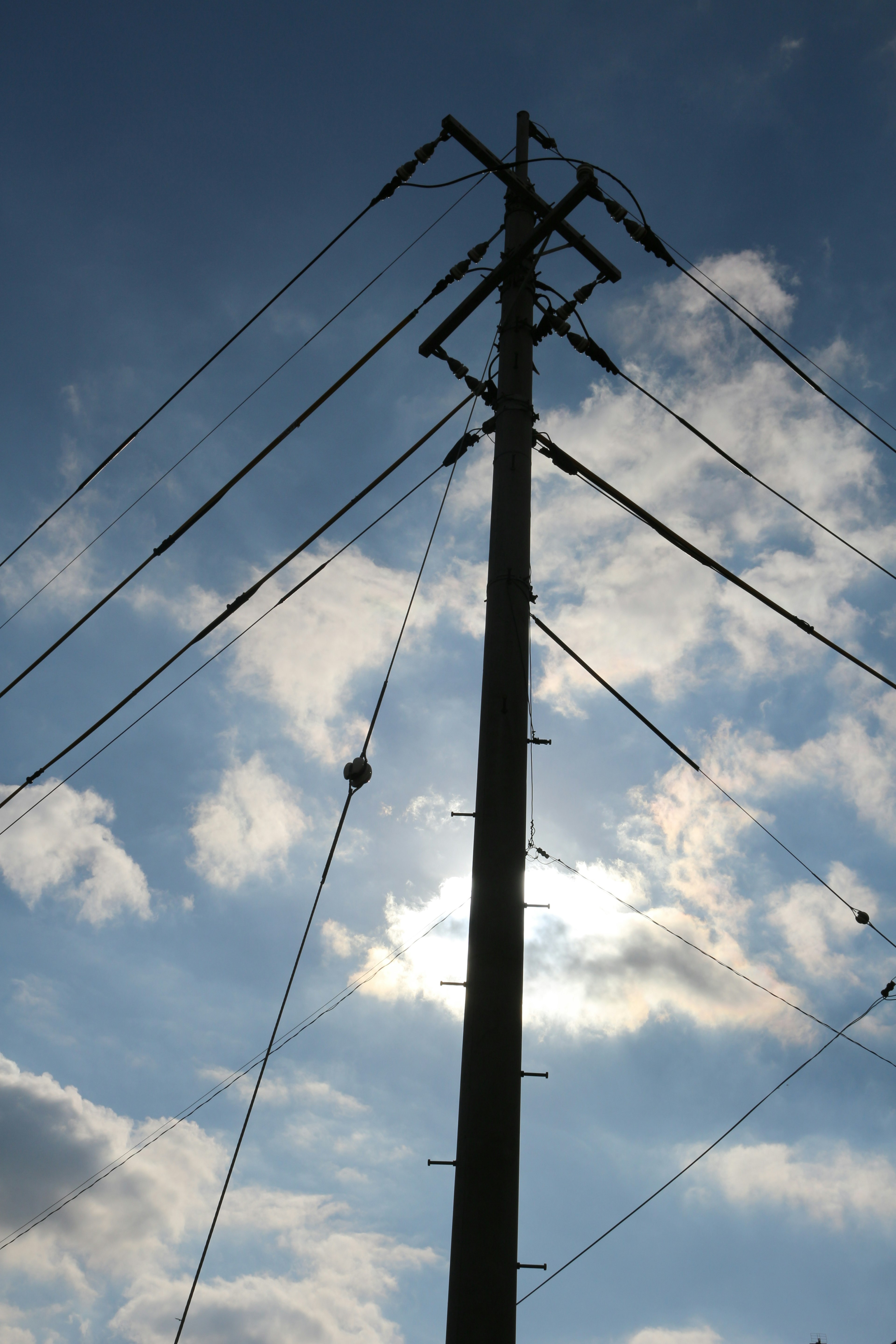 Silhouette of a utility pole against a bright sky with clouds