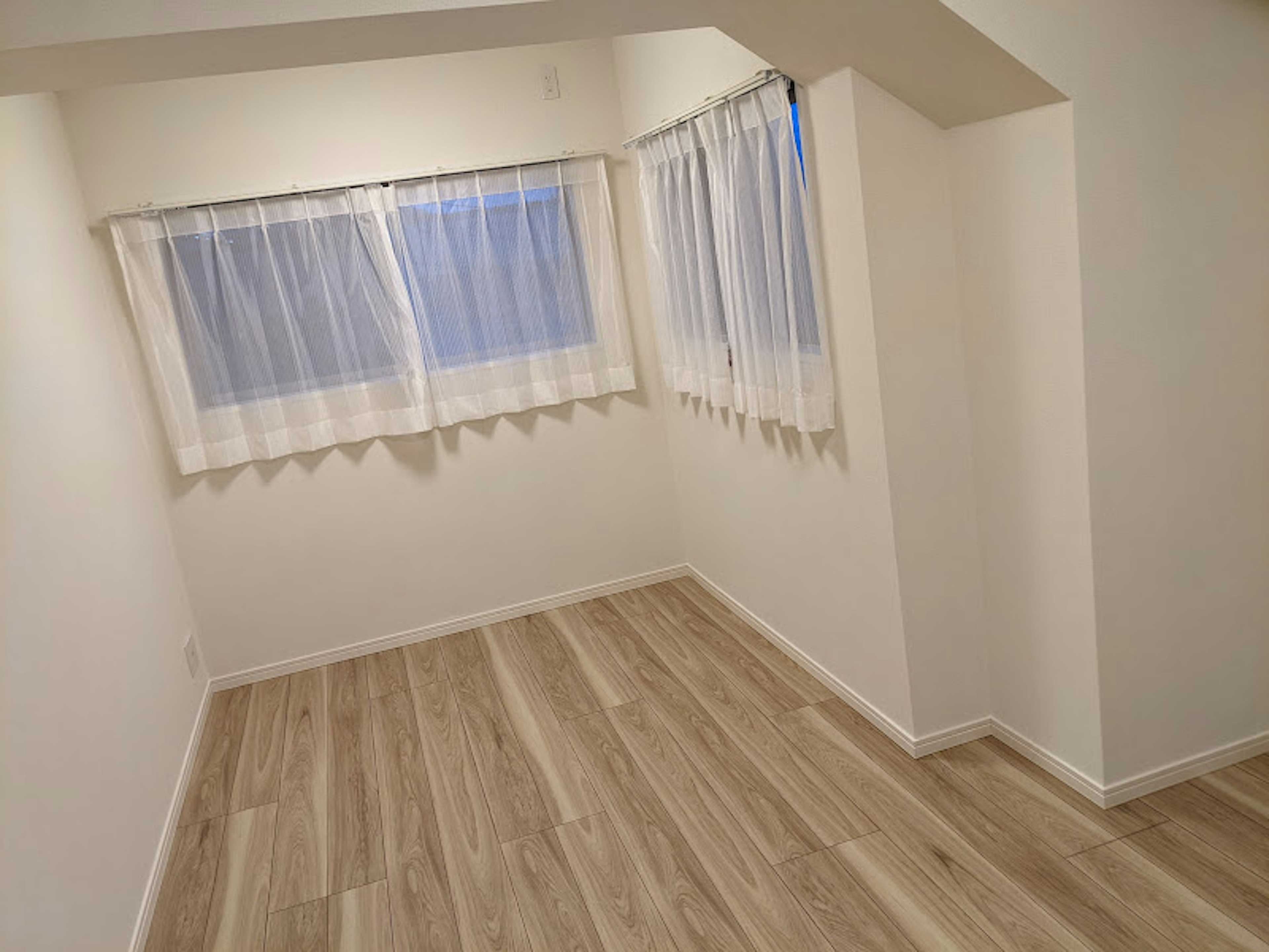 Chambre lumineuse avec des murs blancs et un sol en bois rideaux blancs aux fenêtres