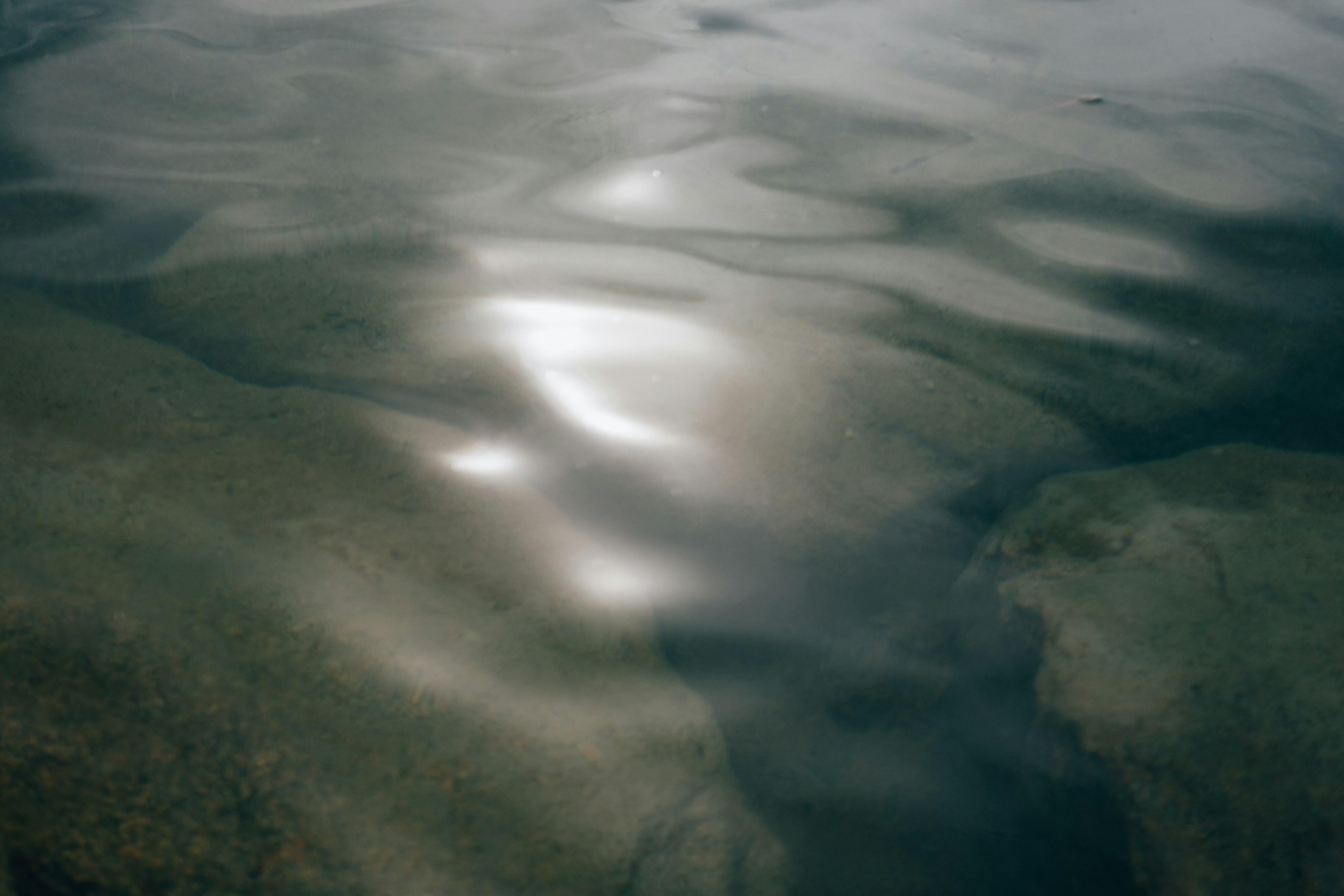 Reflections of light on water surface with smooth rocks underneath