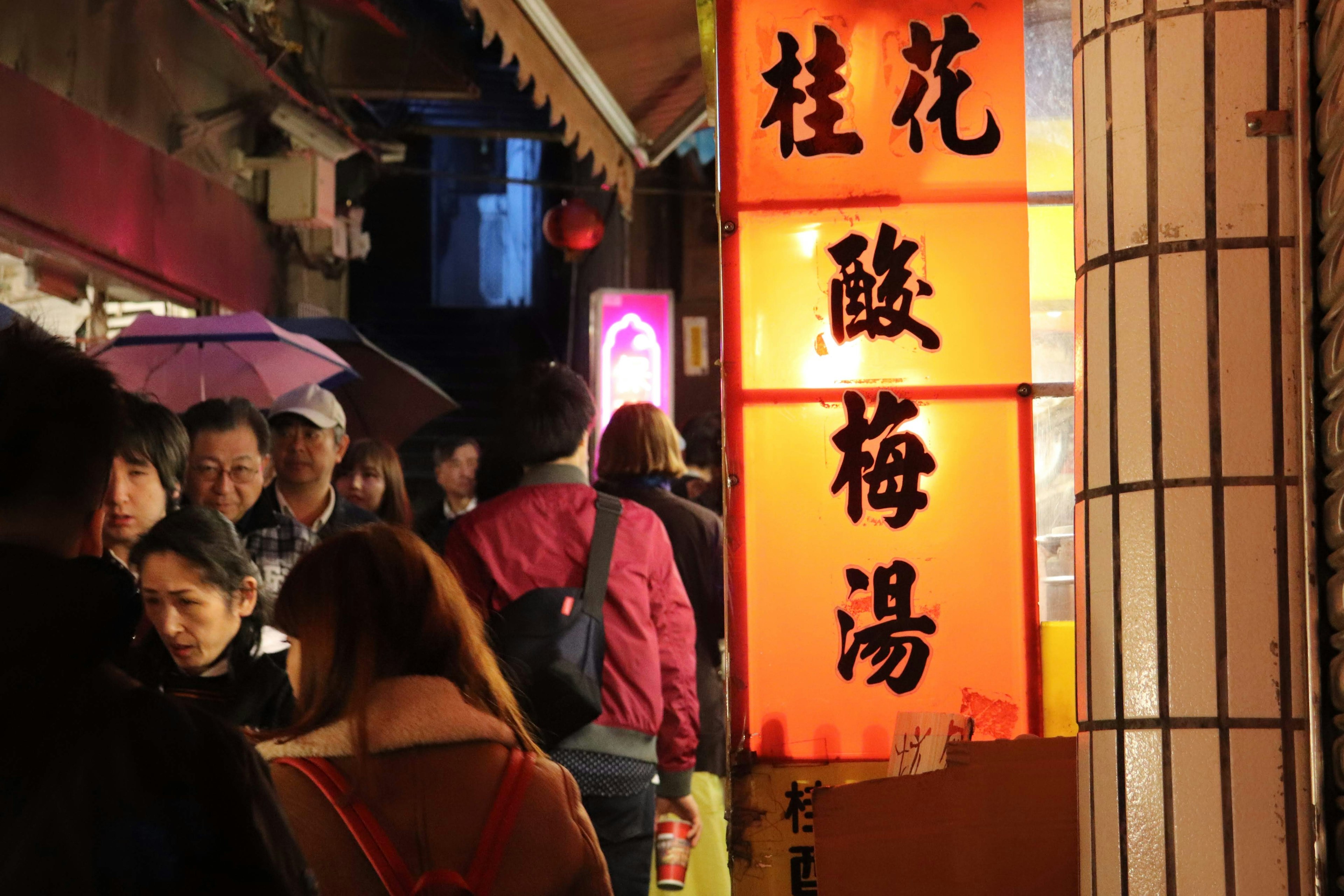 Puesto de comida concurrido en un mercado nocturno con un letrero naranja brillante