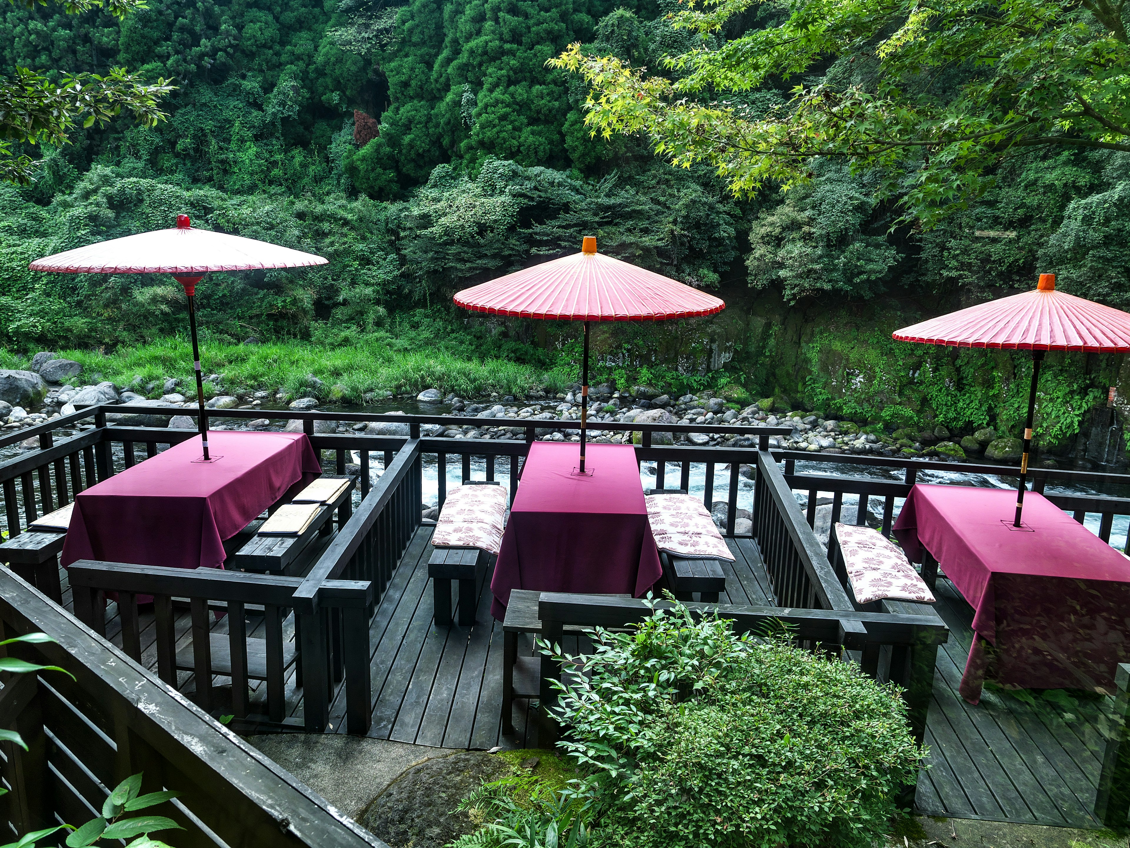 Mesas de restaurante al aire libre junto al río con paraguas rojos