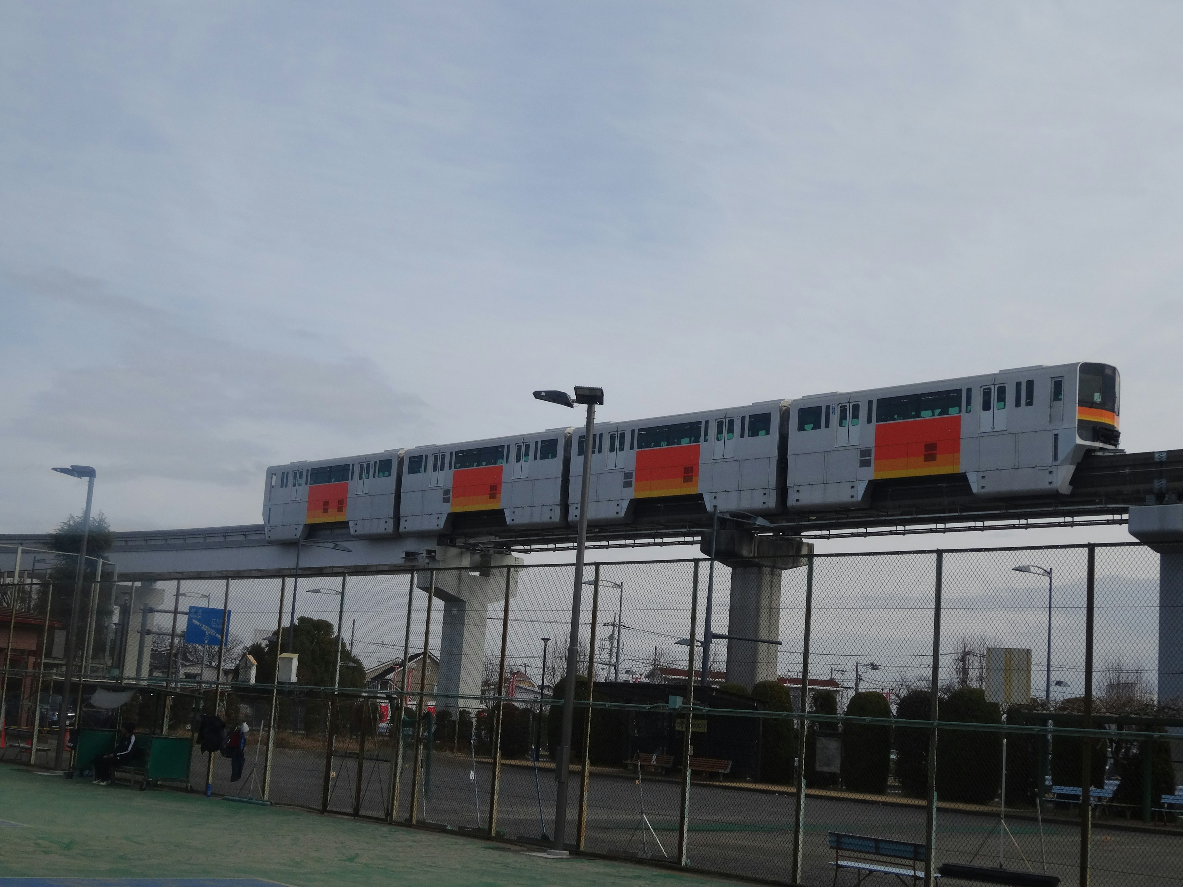 A monorail train elevated above a sports court against a cloudy sky