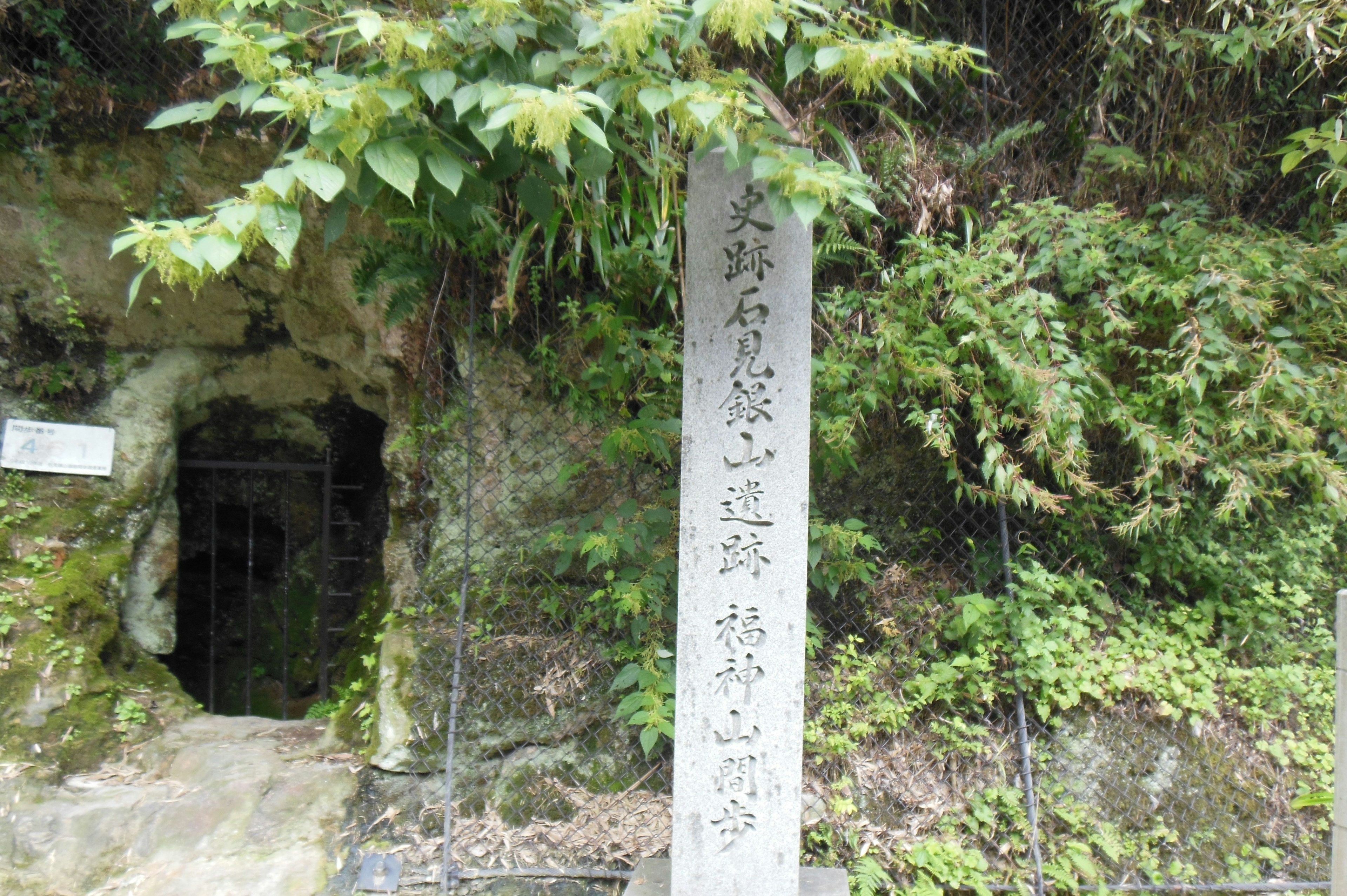 Entrance to a cave with a stone monument surrounded by green foliage