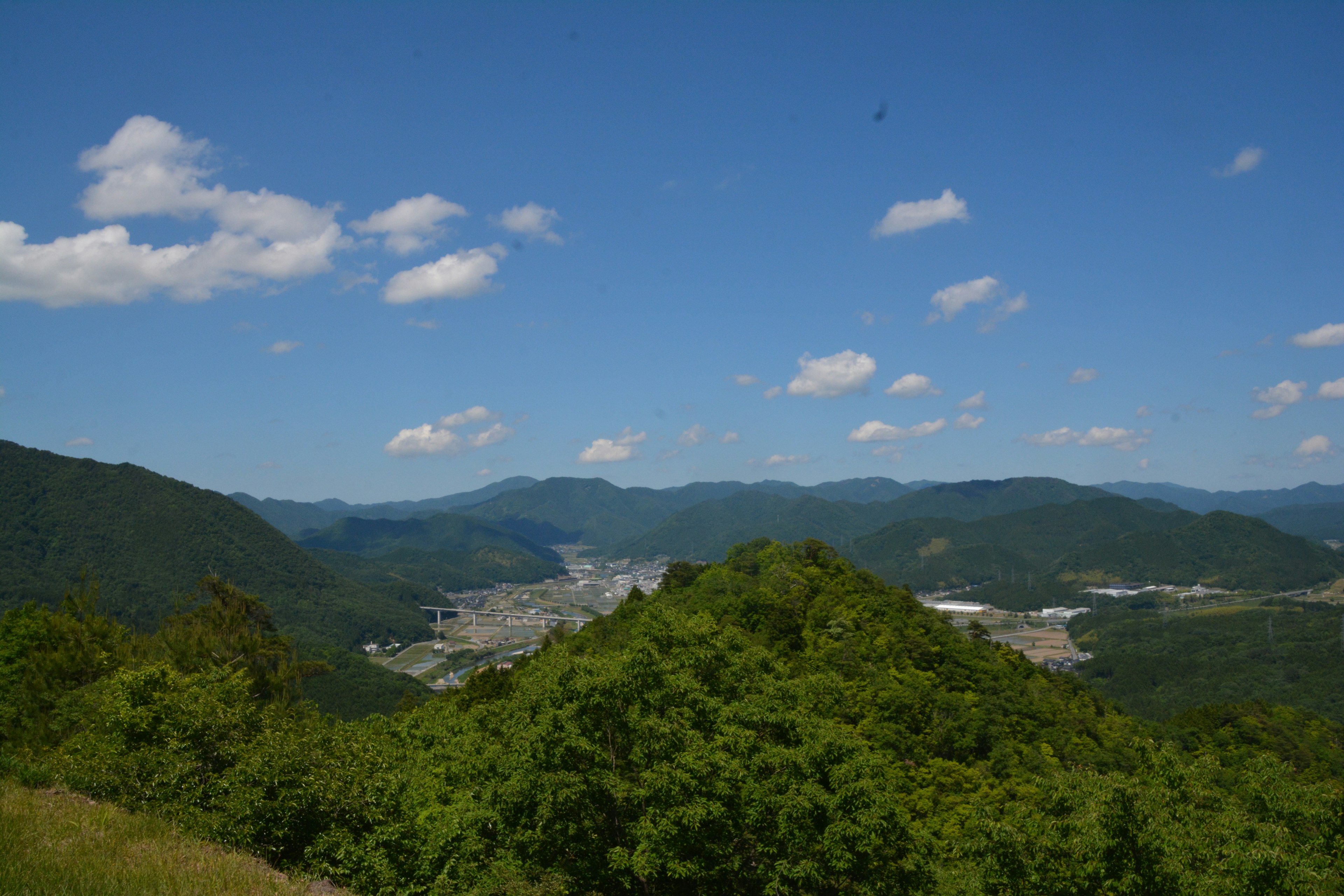 Panoramablick auf grüne Berge unter einem blauen Himmel mit Wolken und einer sichtbaren Stadt