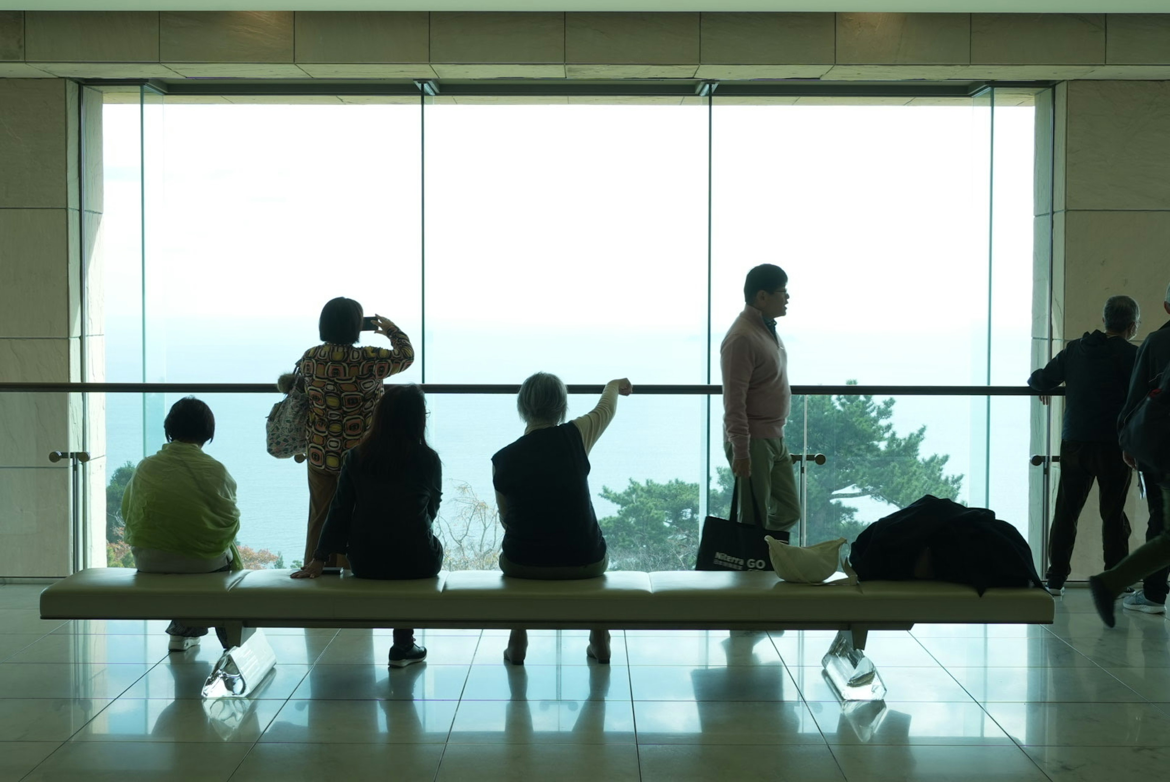 Silhouettes of people sitting by a large window overlooking a distant landscape