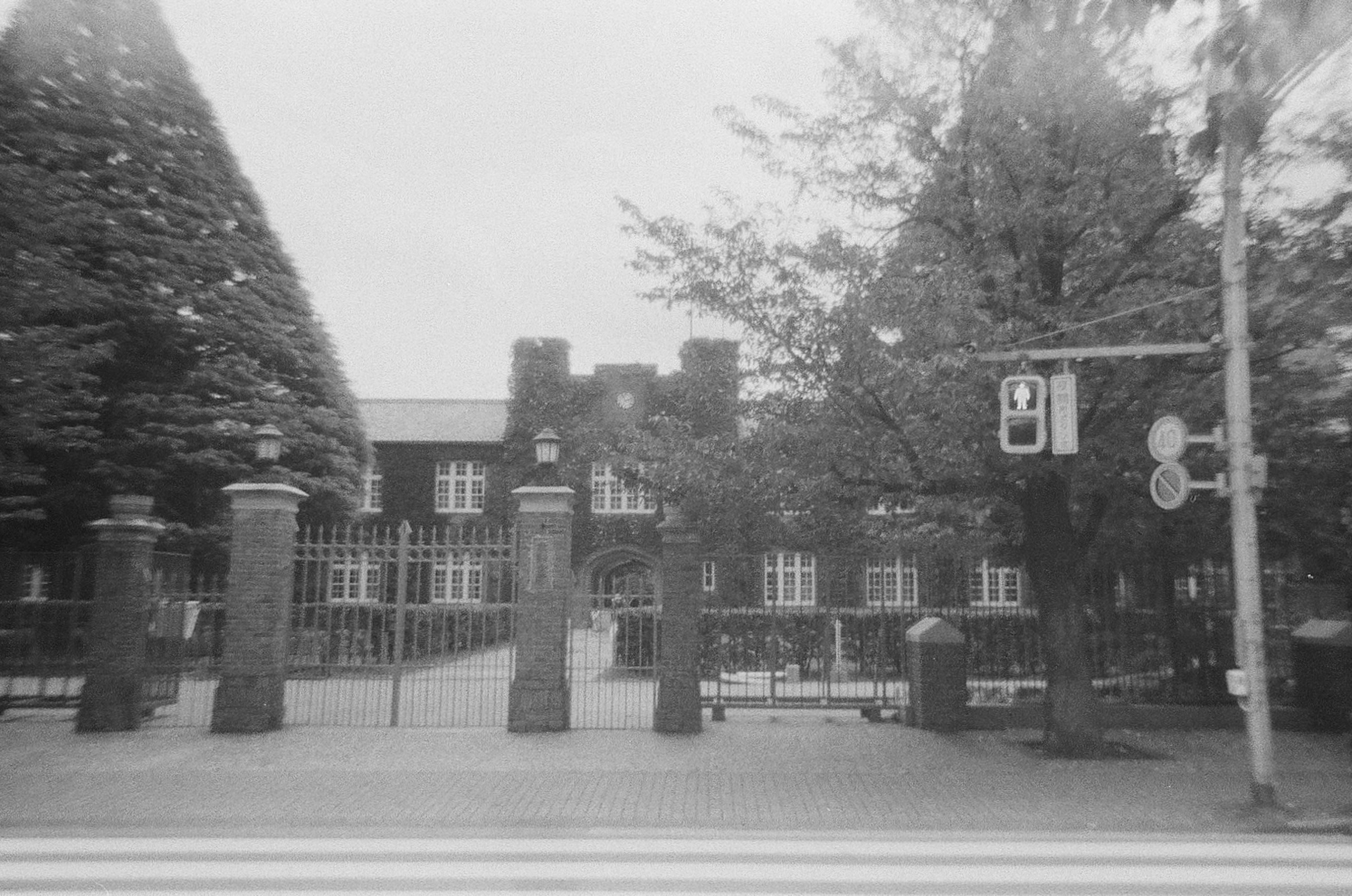 Black and white image of a school entrance with trees and gates