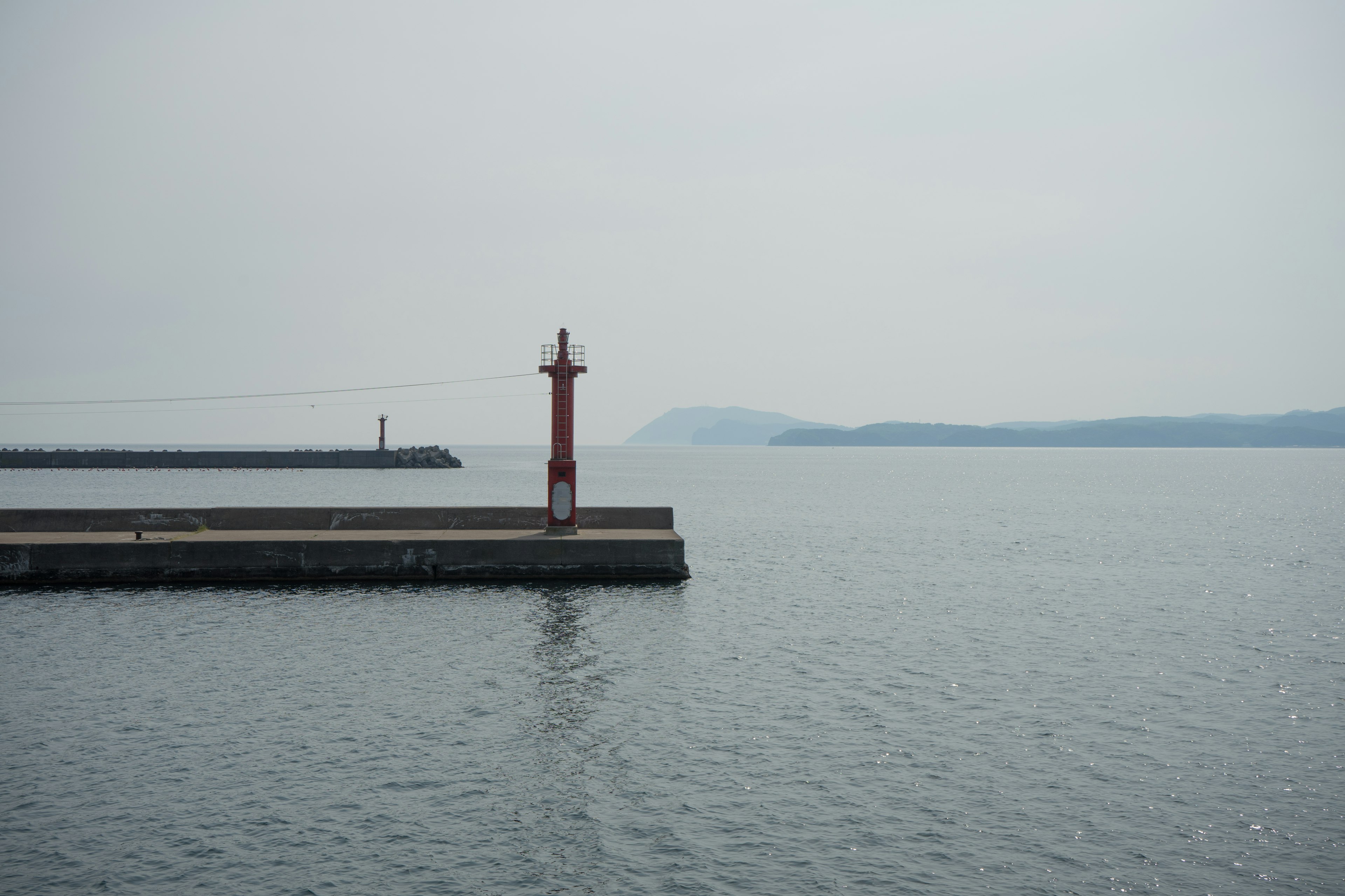 A calm sea with a red lighthouse and pier in the background