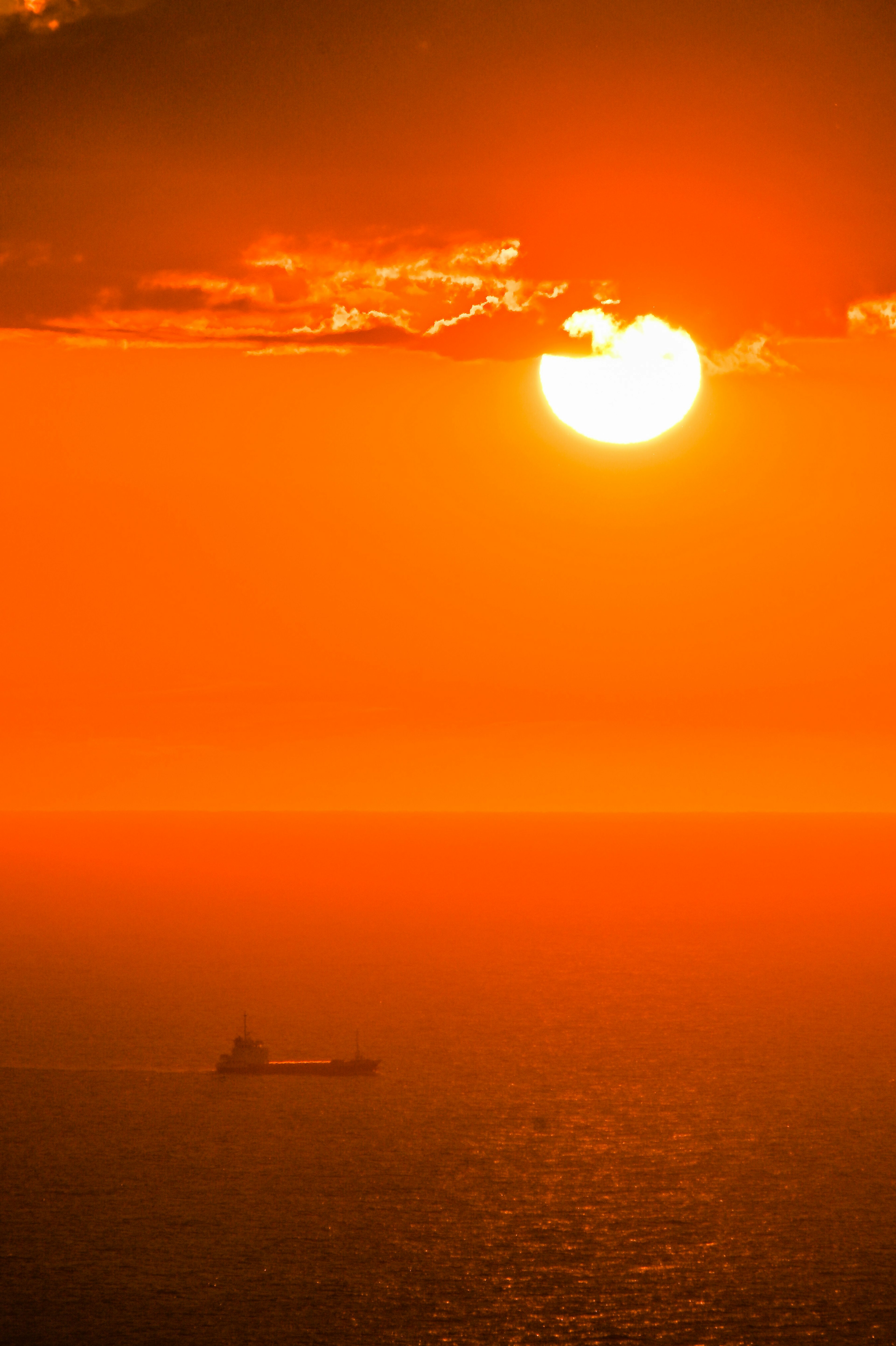 Sonnenuntergang über dem Ozean mit der Silhouette eines Schiffs am Horizont