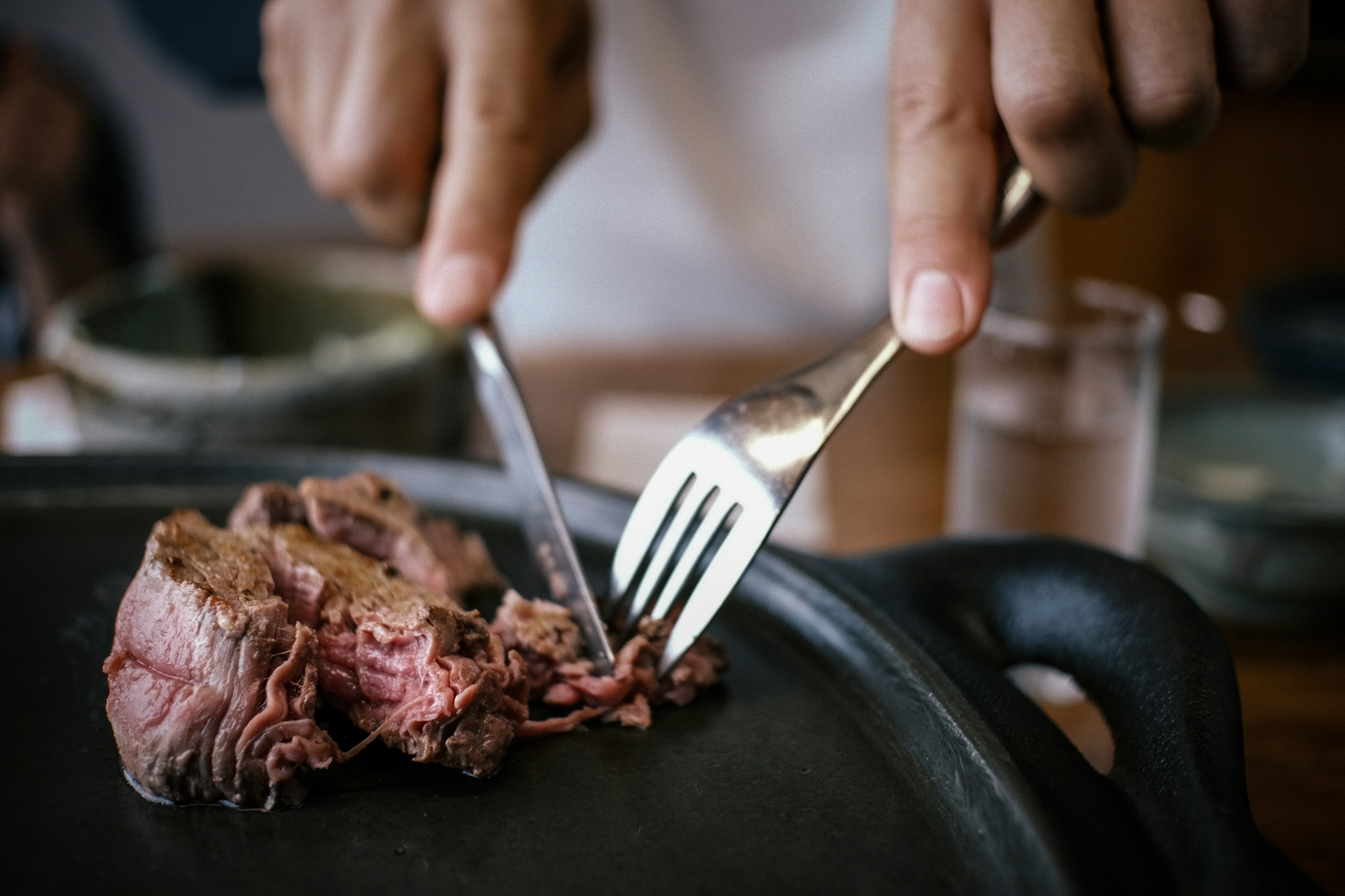 Hands using a knife and fork to cut tender meat on a hot plate