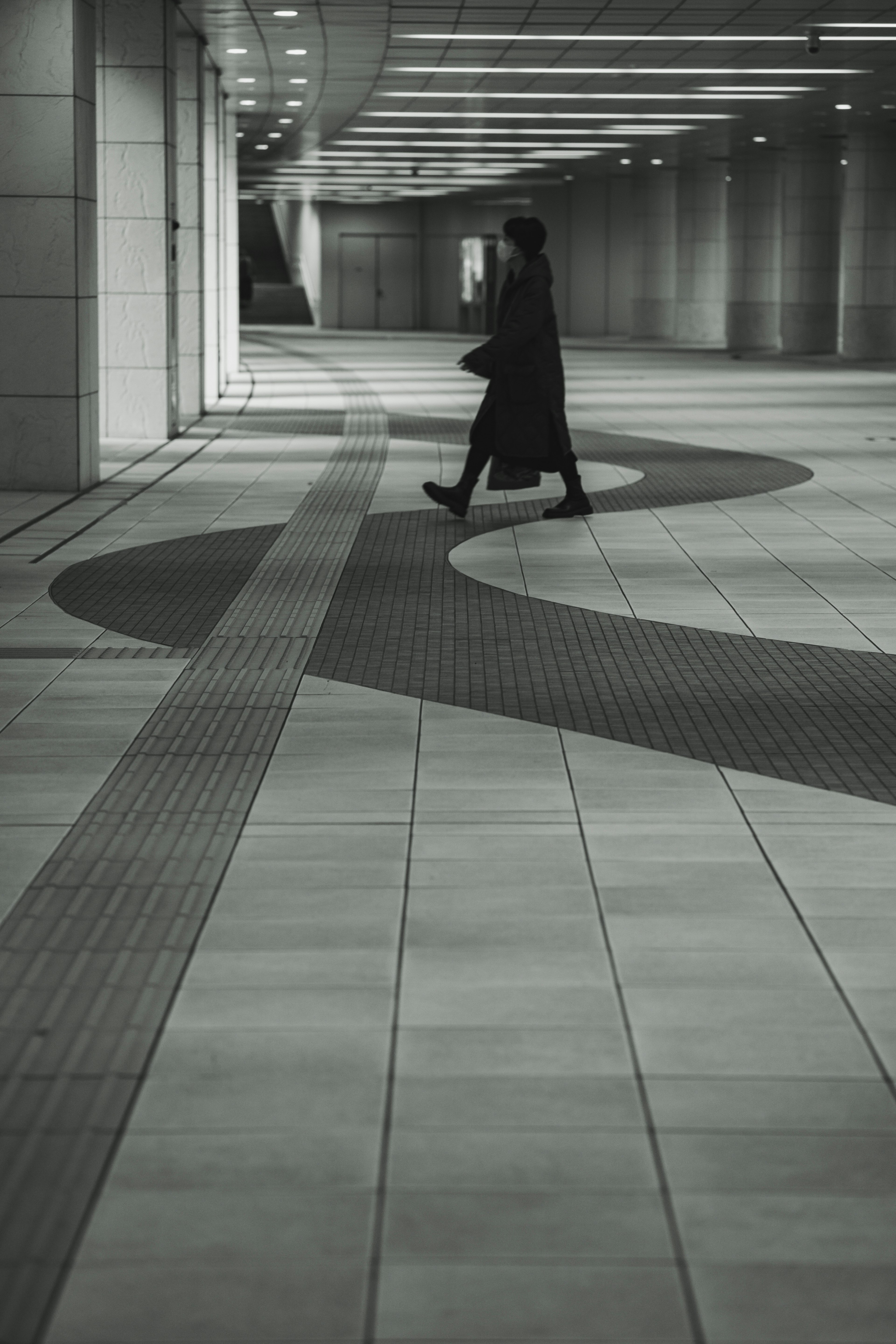 Una escena urbana en blanco y negro con una figura en un abrigo negro caminando por un camino sinuoso