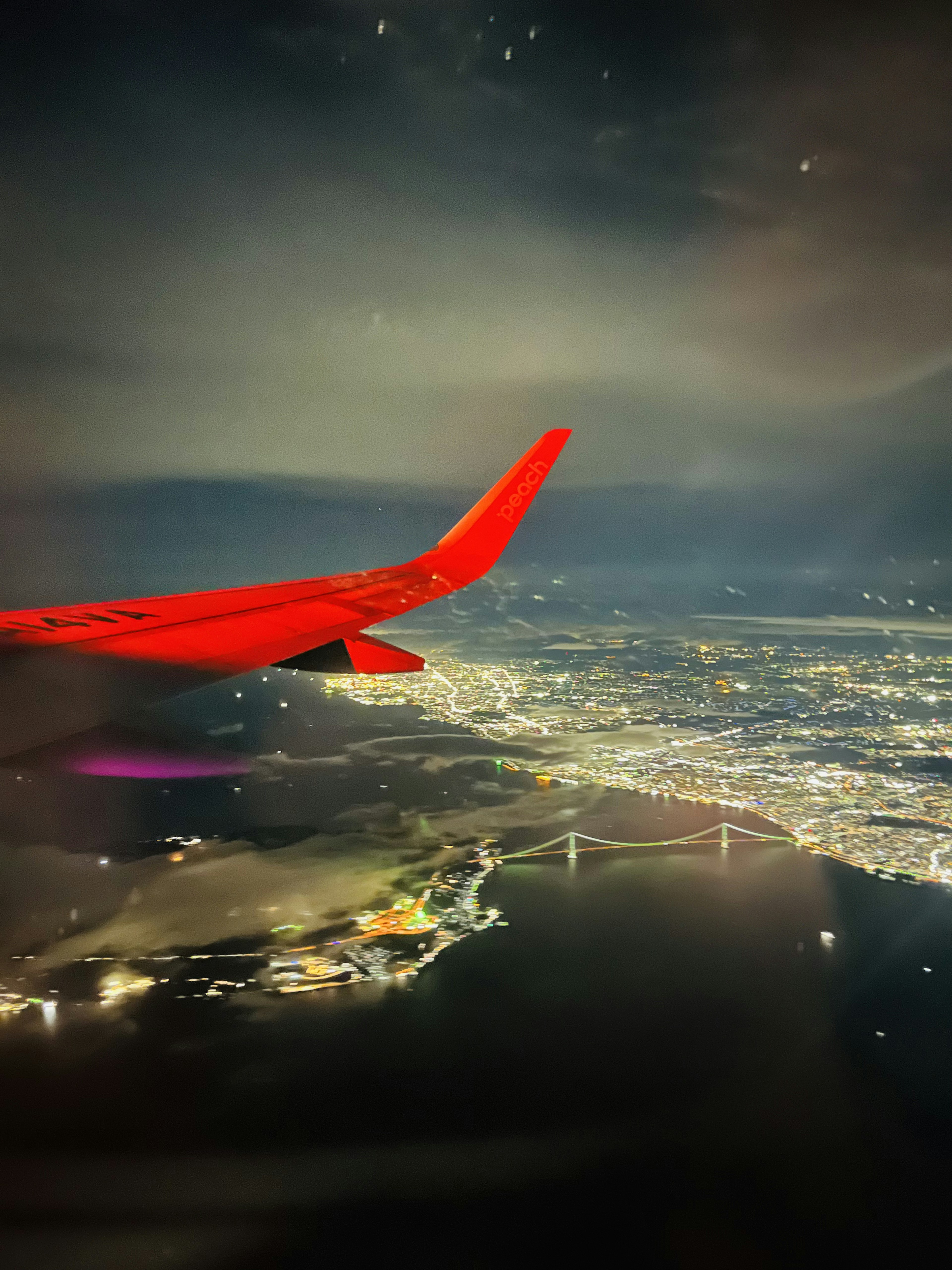 夜空に浮かぶ飛行機の翼と明るい都市の景色