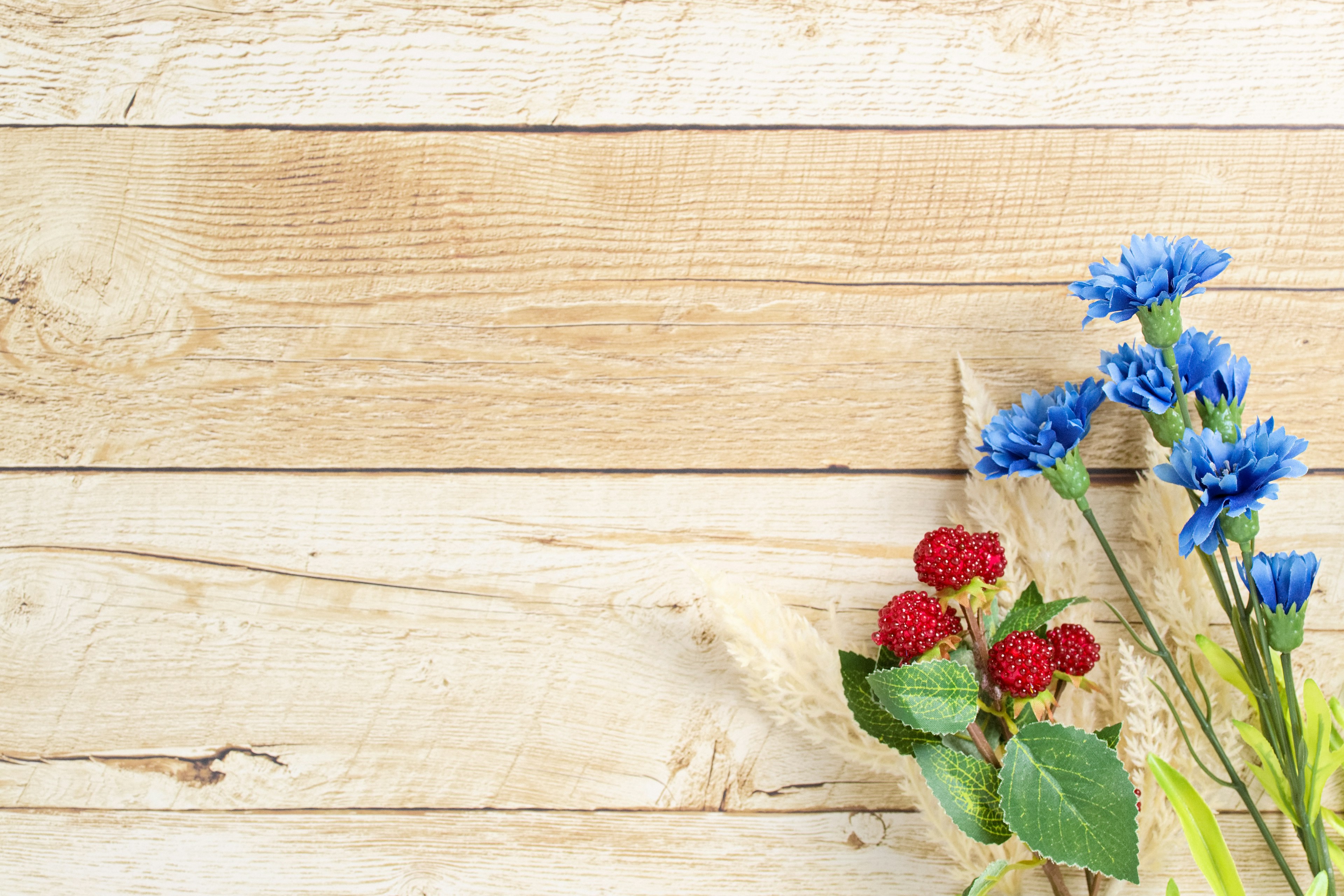 Eine ruhige Anordnung von blauen Blumen und roten Beeren auf einem Holzuntergrund