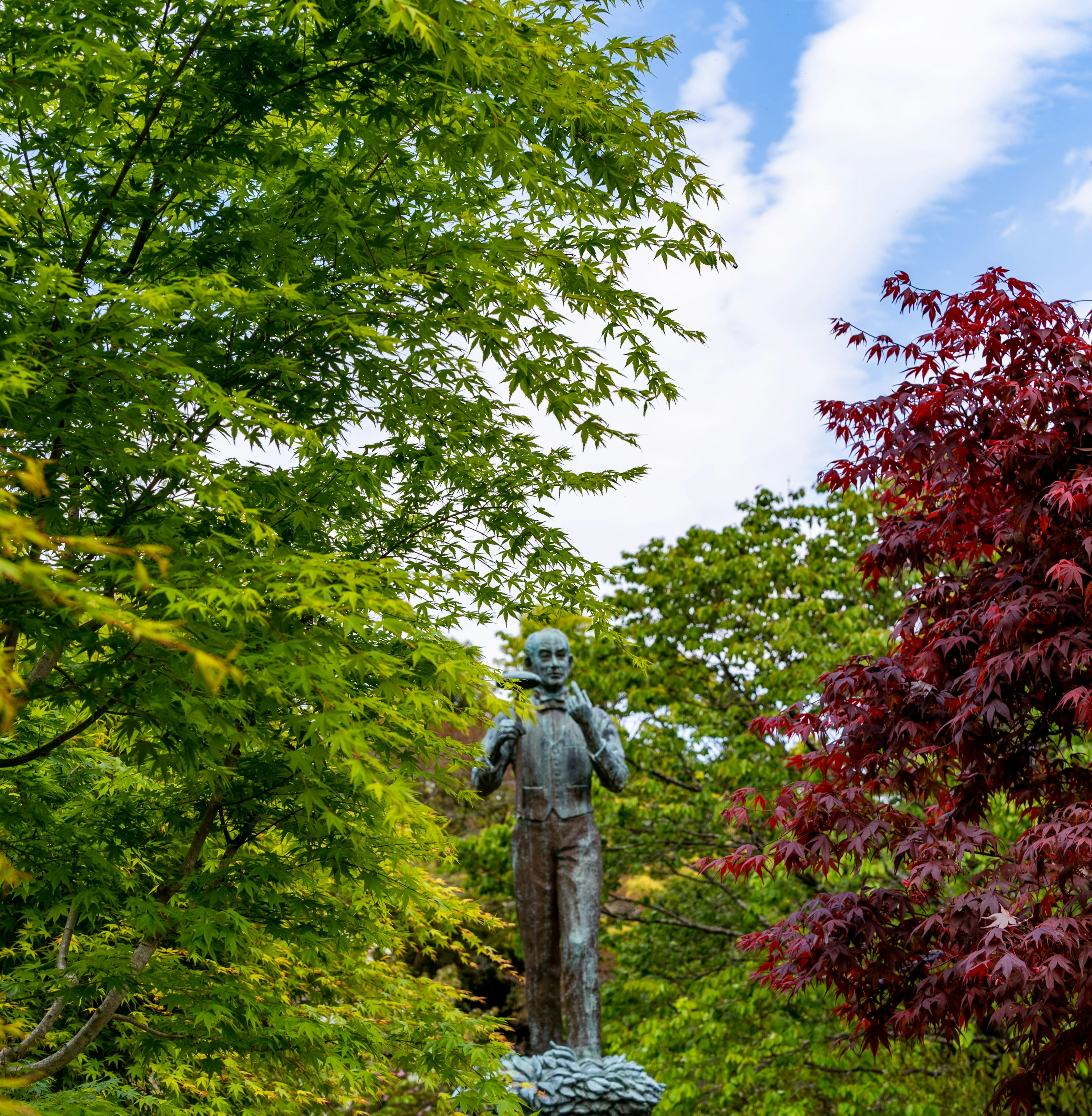 Estatua de bronce de pie en un parque exuberante rodeada de árboles coloridos