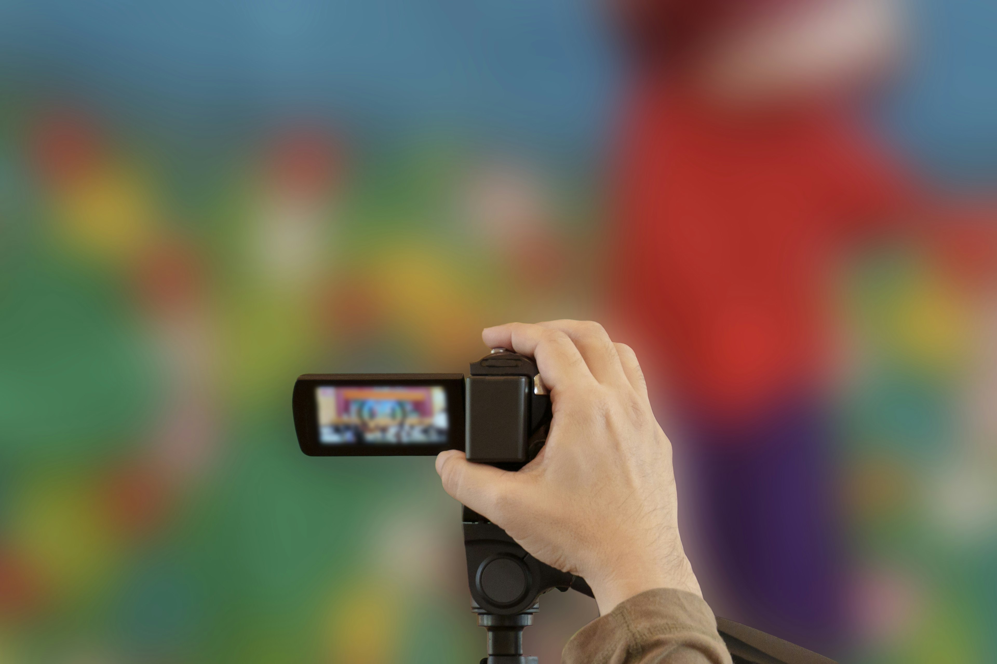 Blurred image of a person holding a camera with colorful flowers in the background