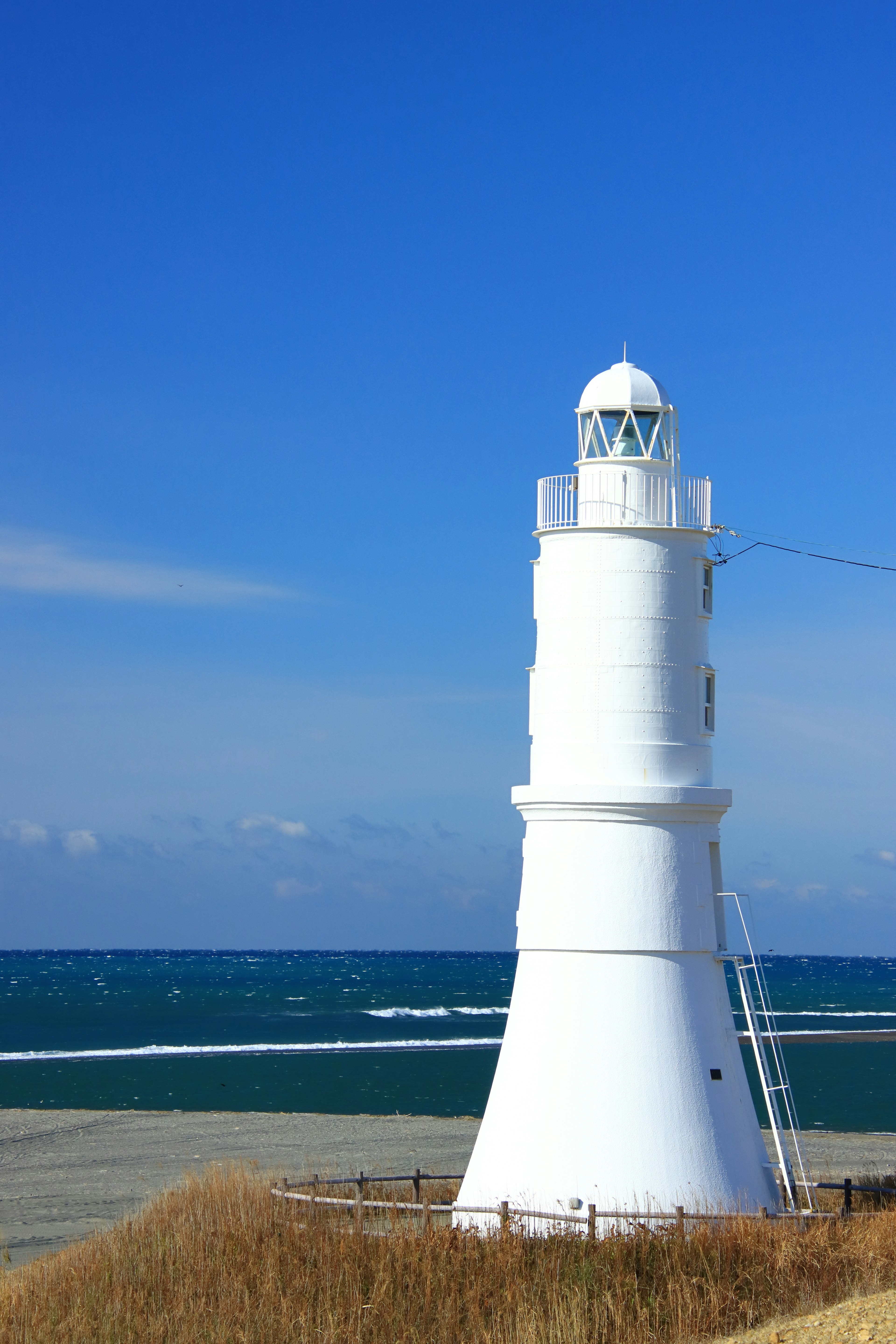 Weißer Leuchtturm vor blauem Meer und klarem Himmel