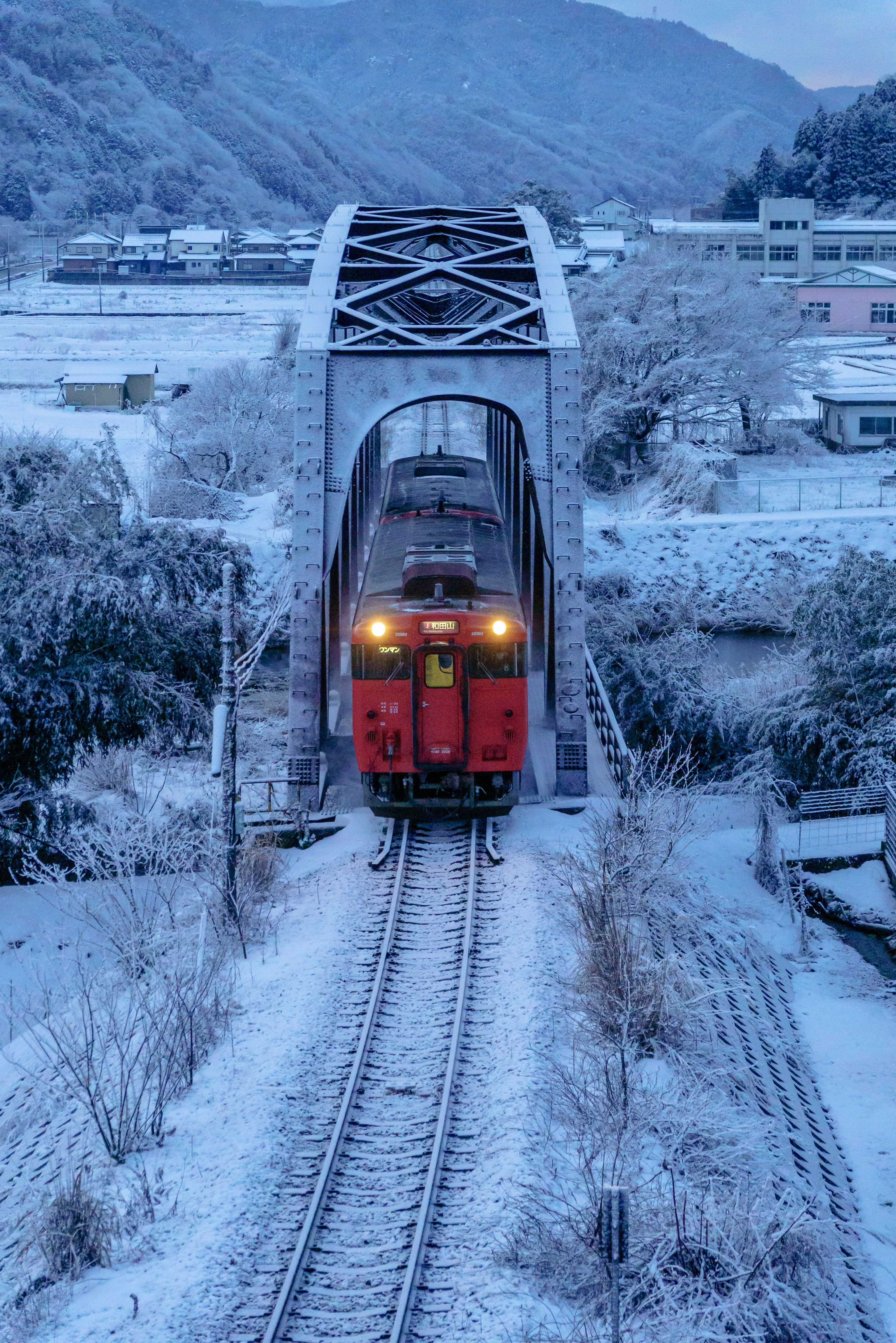 รถไฟสีแดงข้ามสะพานรถไฟที่ปกคลุมด้วยหิมะ