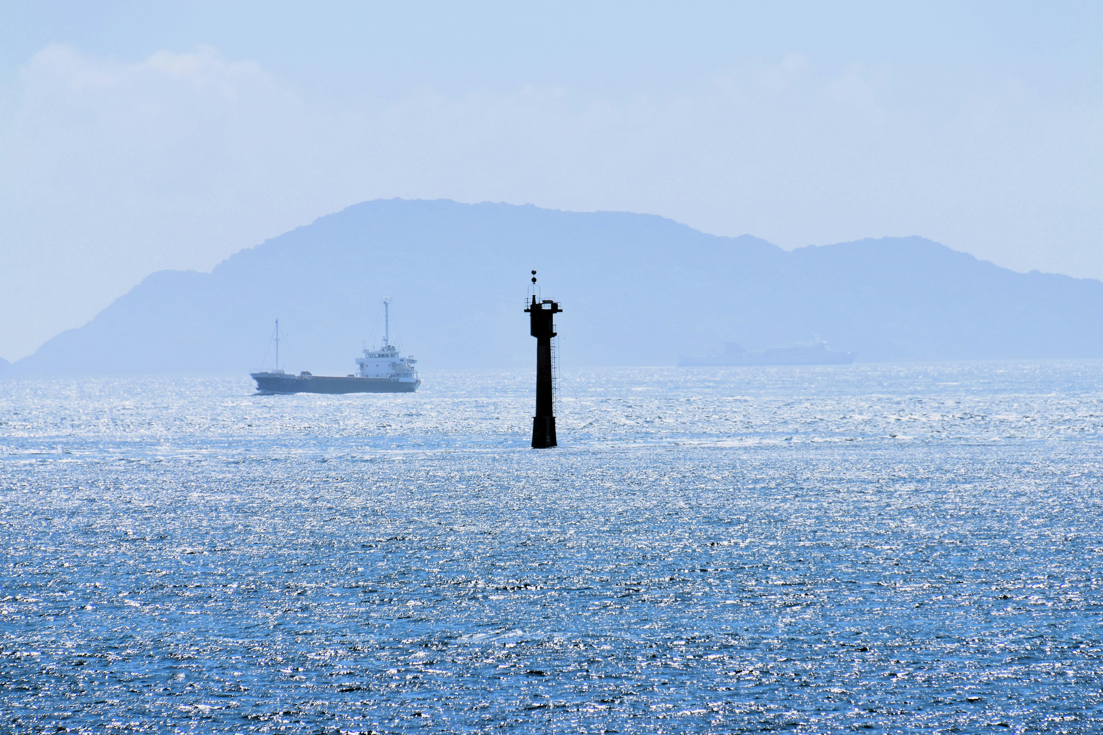 Mercusuar di atas air dengan kapal dan pulau jauh