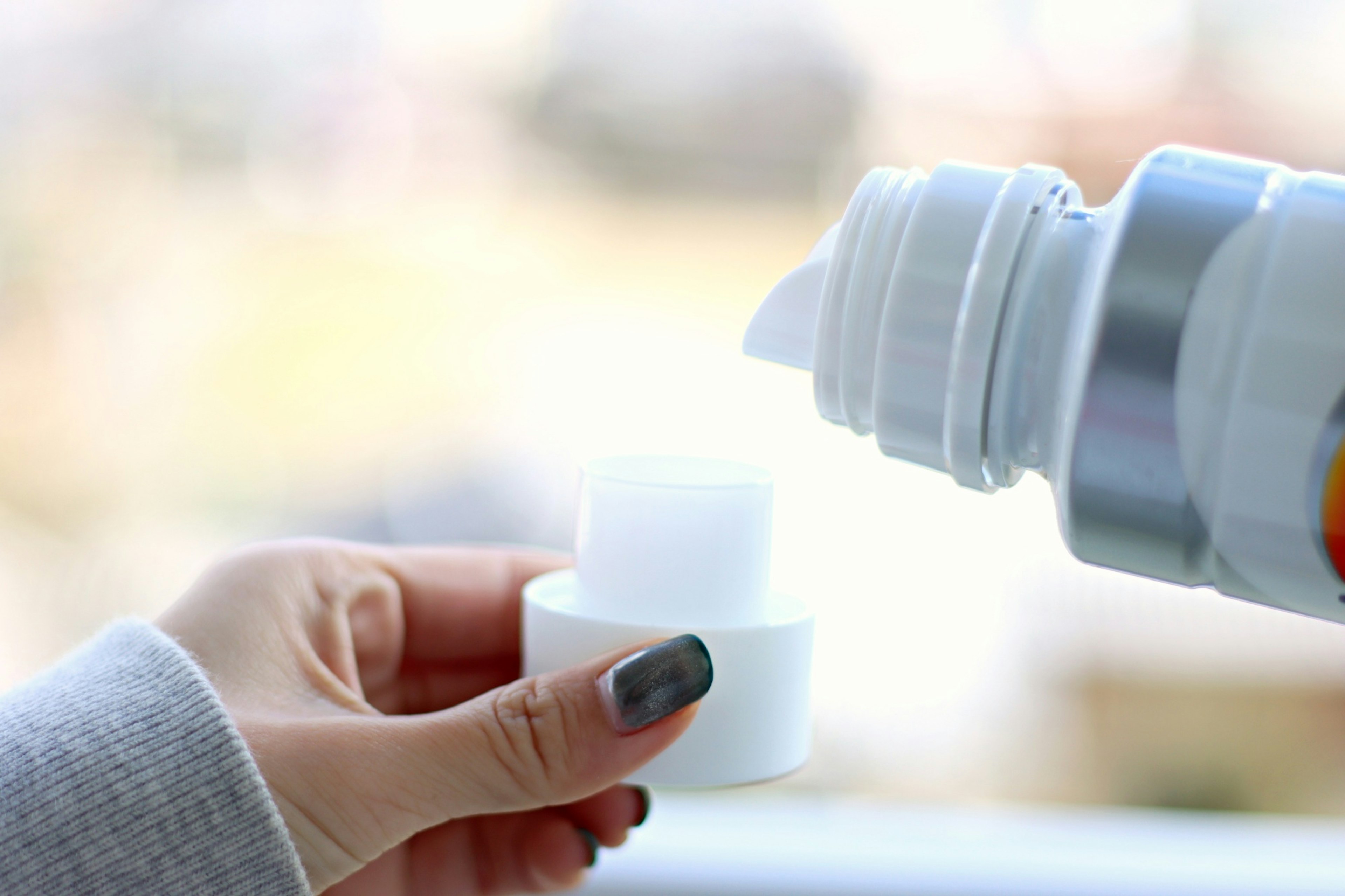 Eine Hand, die Flüssigkeit aus einer weißen Flasche in einen Deckel gießt