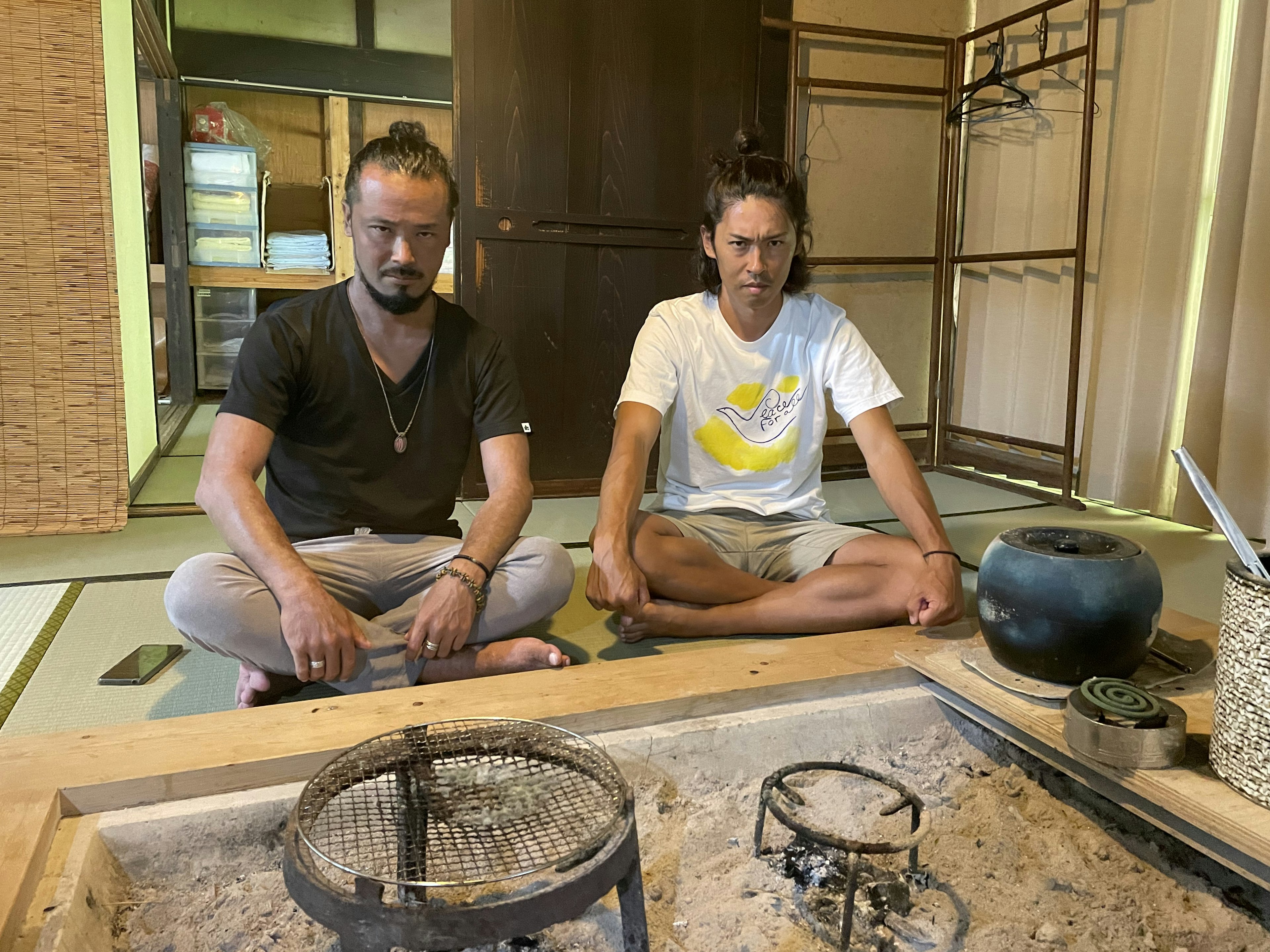 Dos hombres sentados en una habitación de estilo japonés con un hogar hundido visible