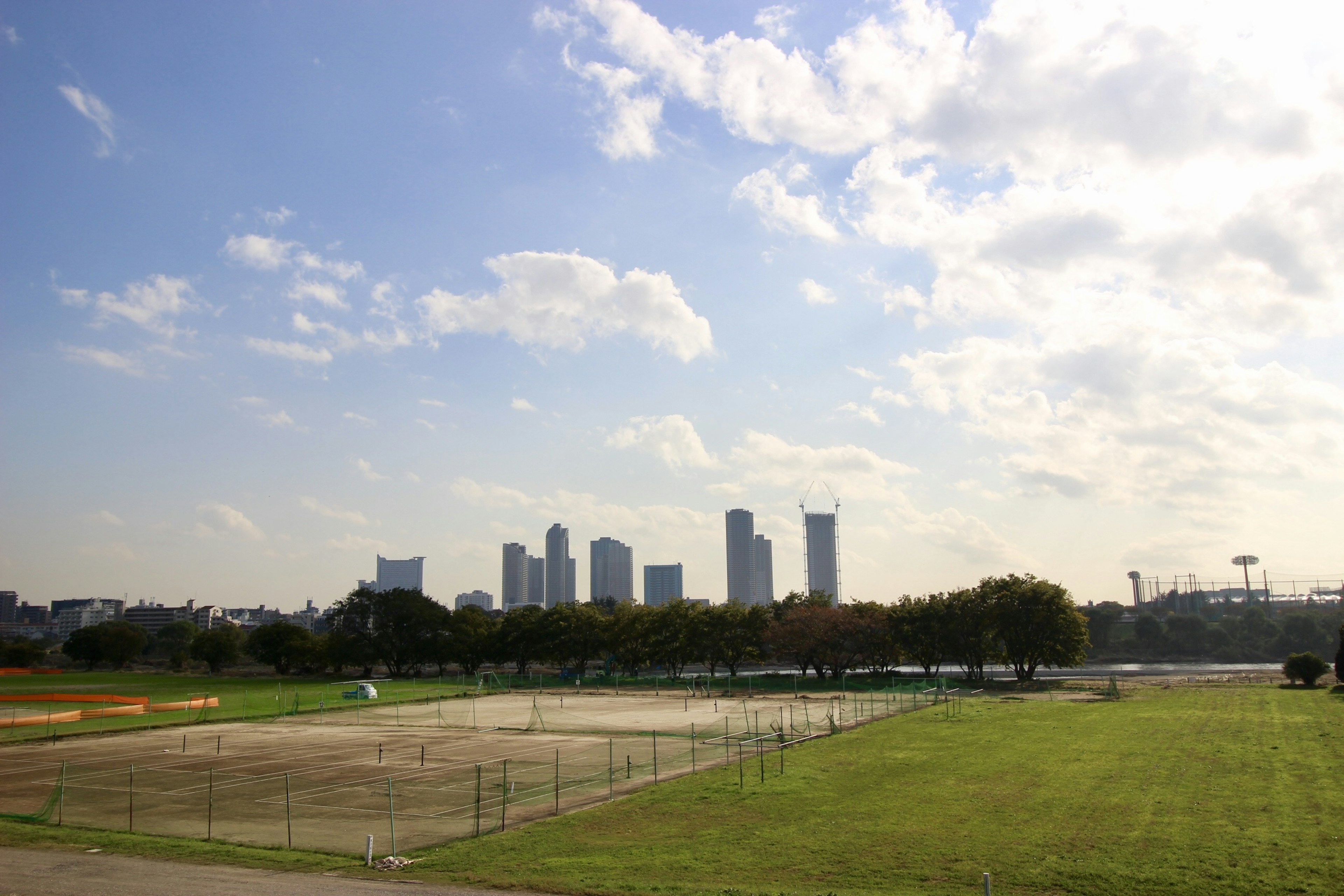 Garis langit kota dengan lapangan hijau dan lapangan tenis di latar depan