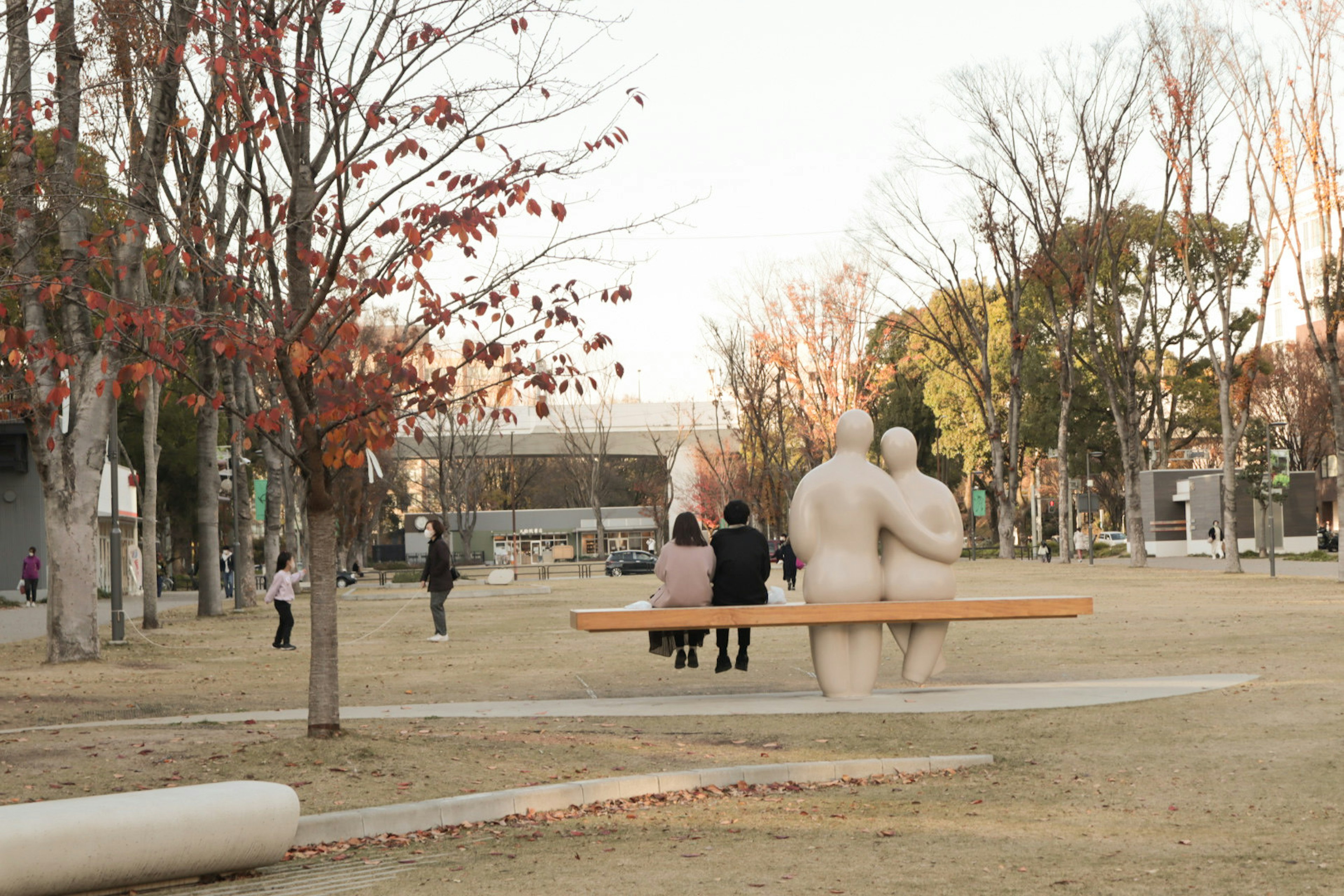 公園にある人間の彫刻とベンチを背にしたカップル