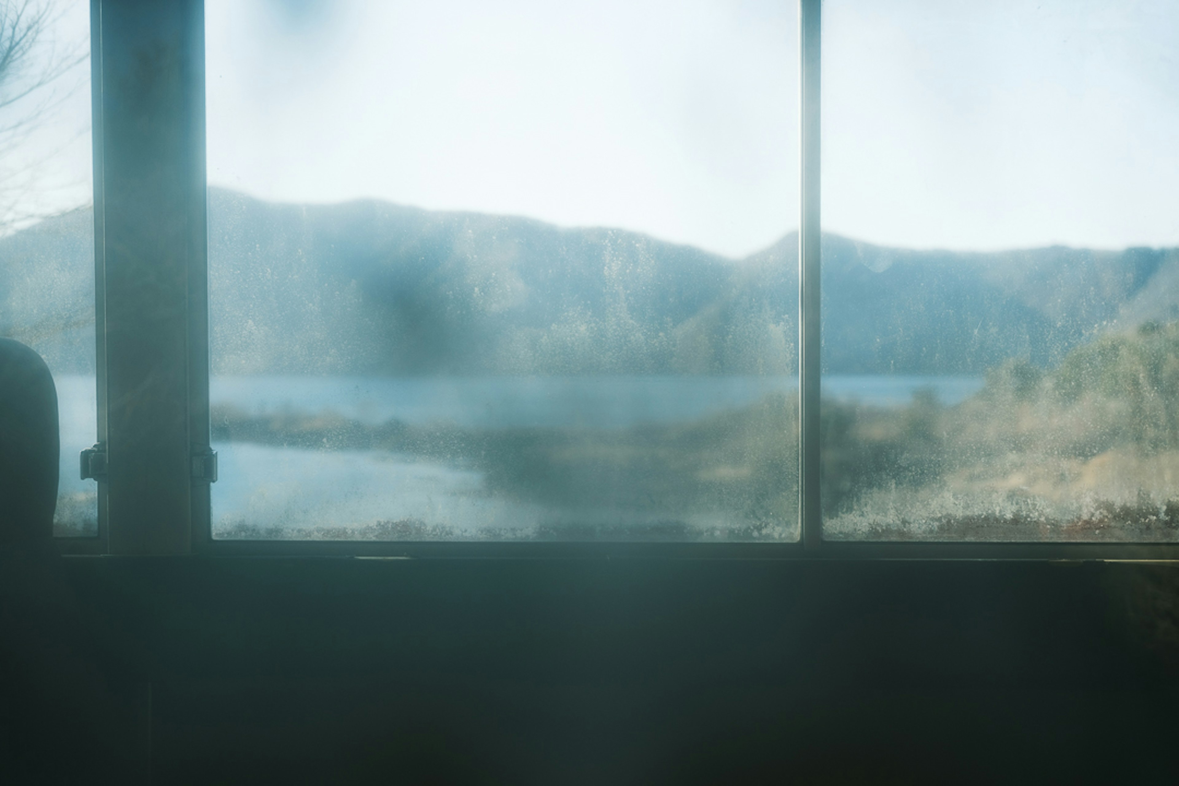 Blick auf einen See und Berge durch ein beschlagenes Fenster