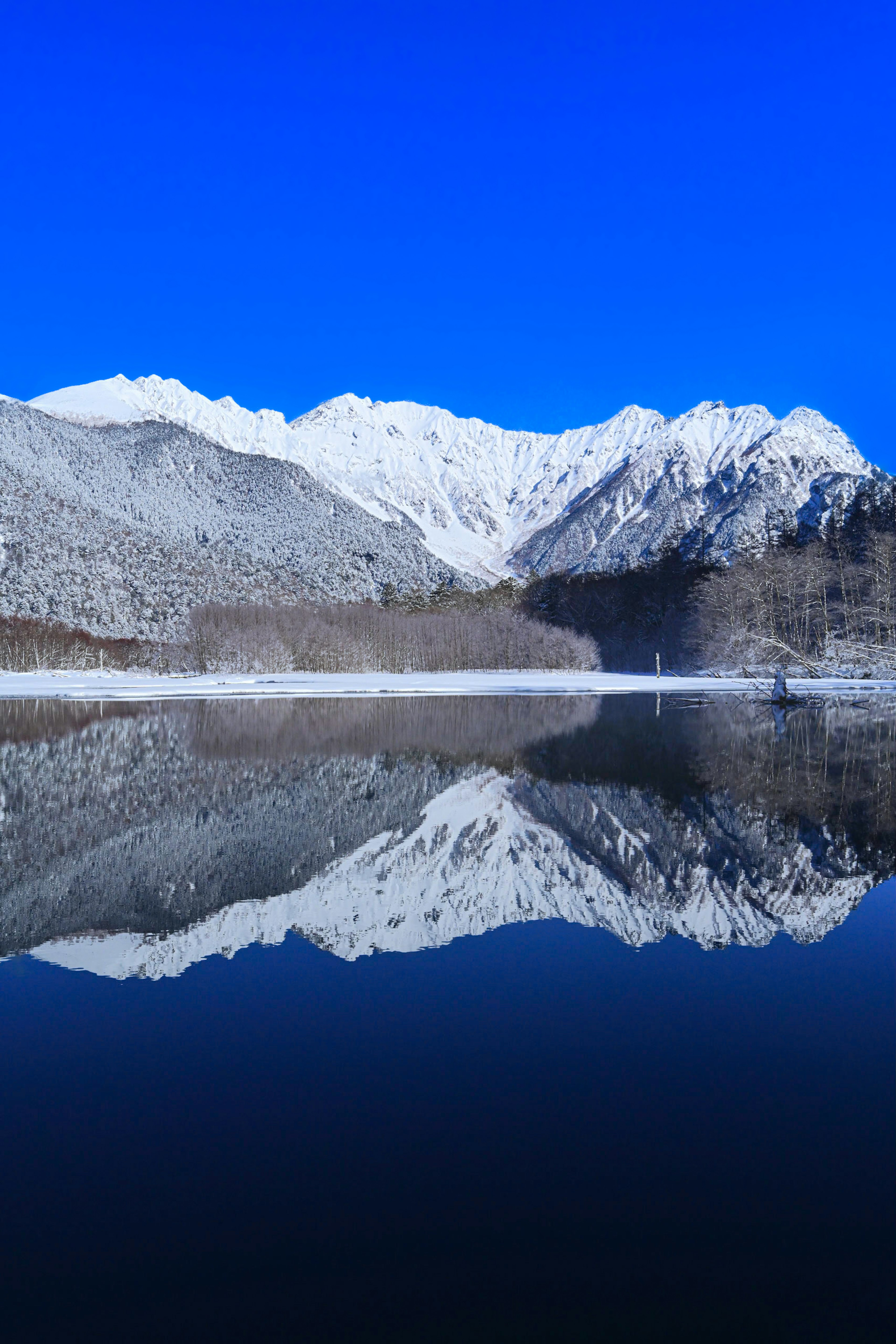 Scenic view of snow-covered mountains reflecting in a lake under a clear blue sky