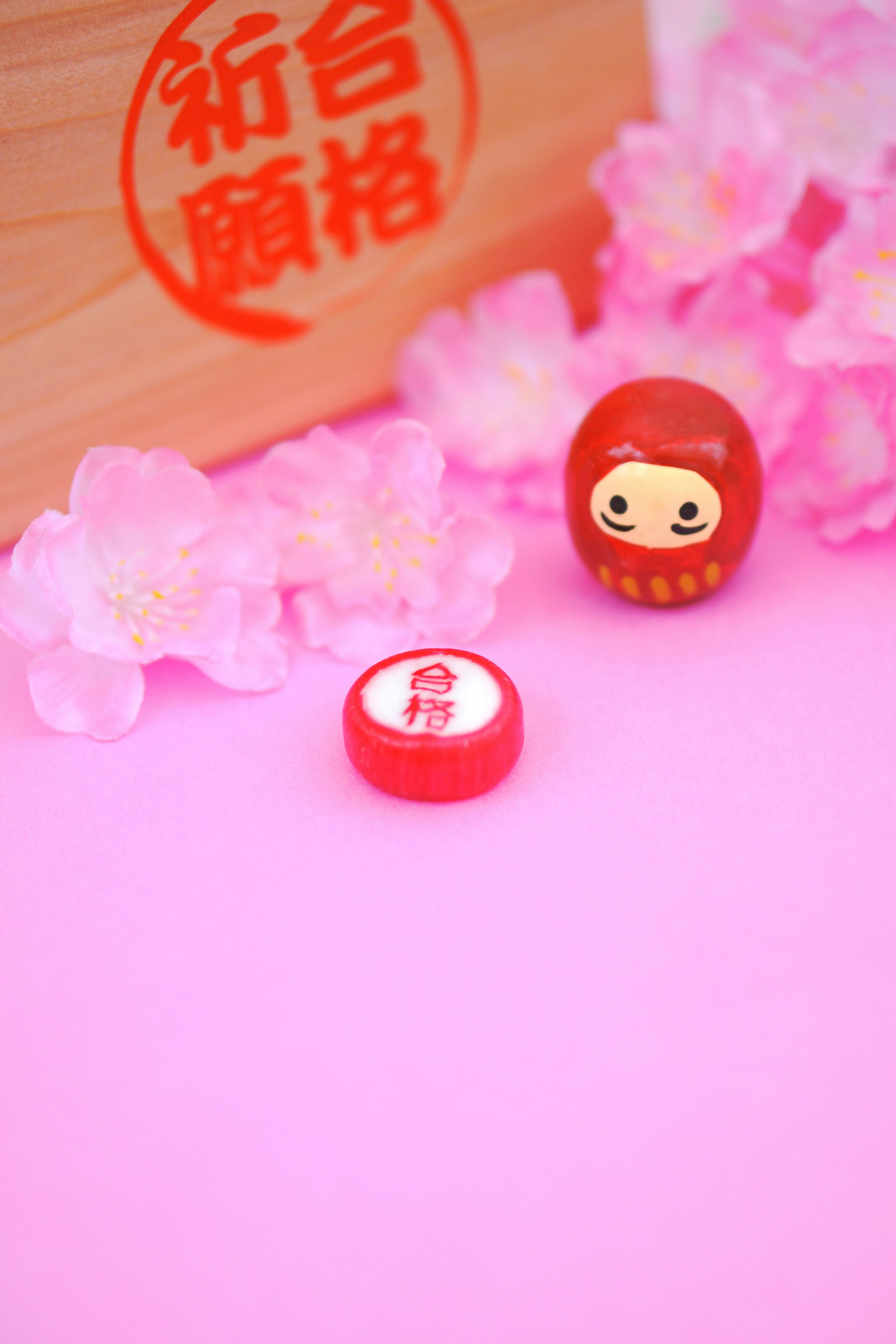 Rote Daruma-Puppe und rotes Bonbon auf rosa Hintergrund mit Kirschblüten