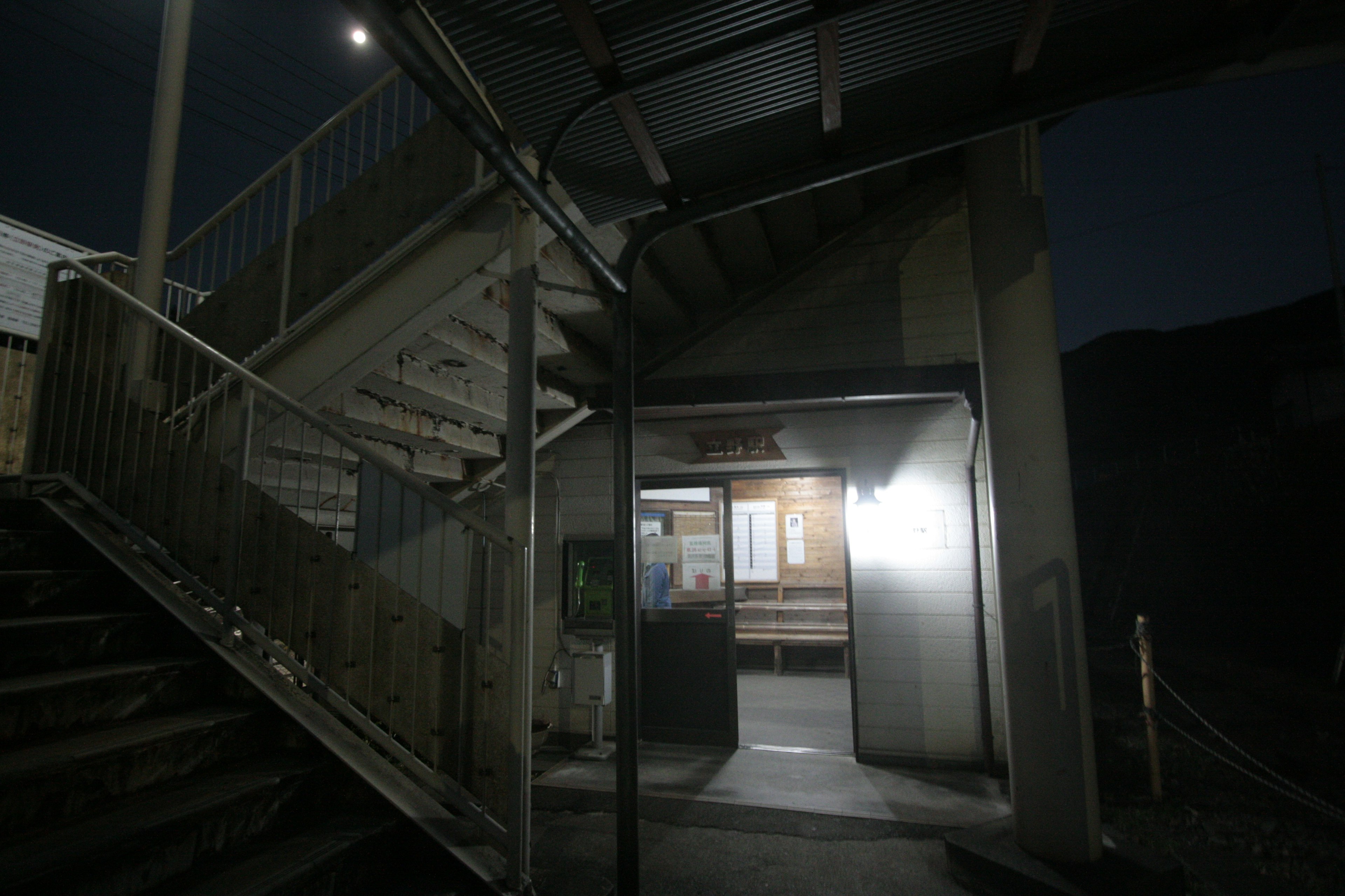 Entrée faiblement éclairée avec pièce illuminée sous un escalier