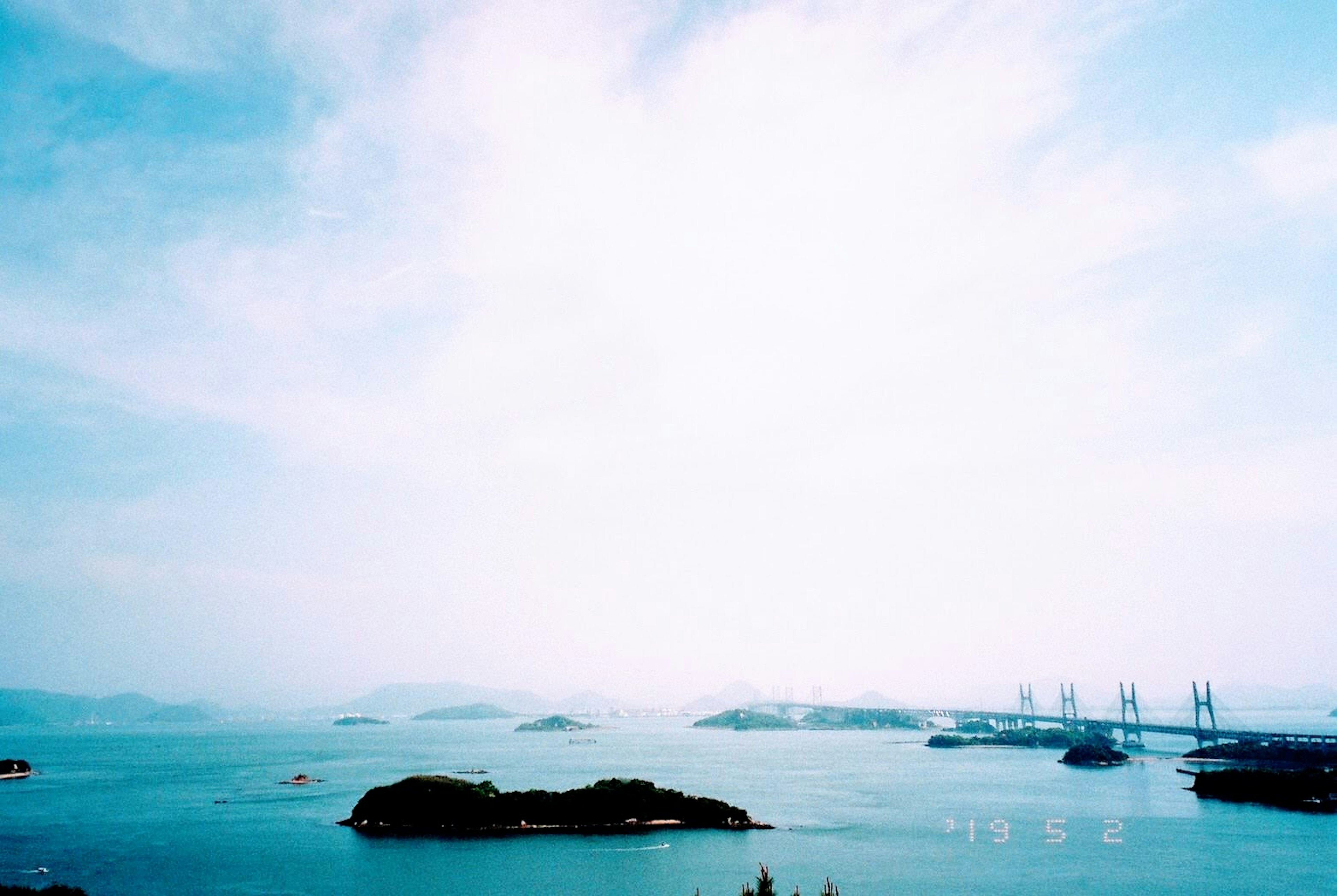 Pemandangan panorama laut biru dengan pulau kecil dan jembatan di kejauhan di bawah langit cerah