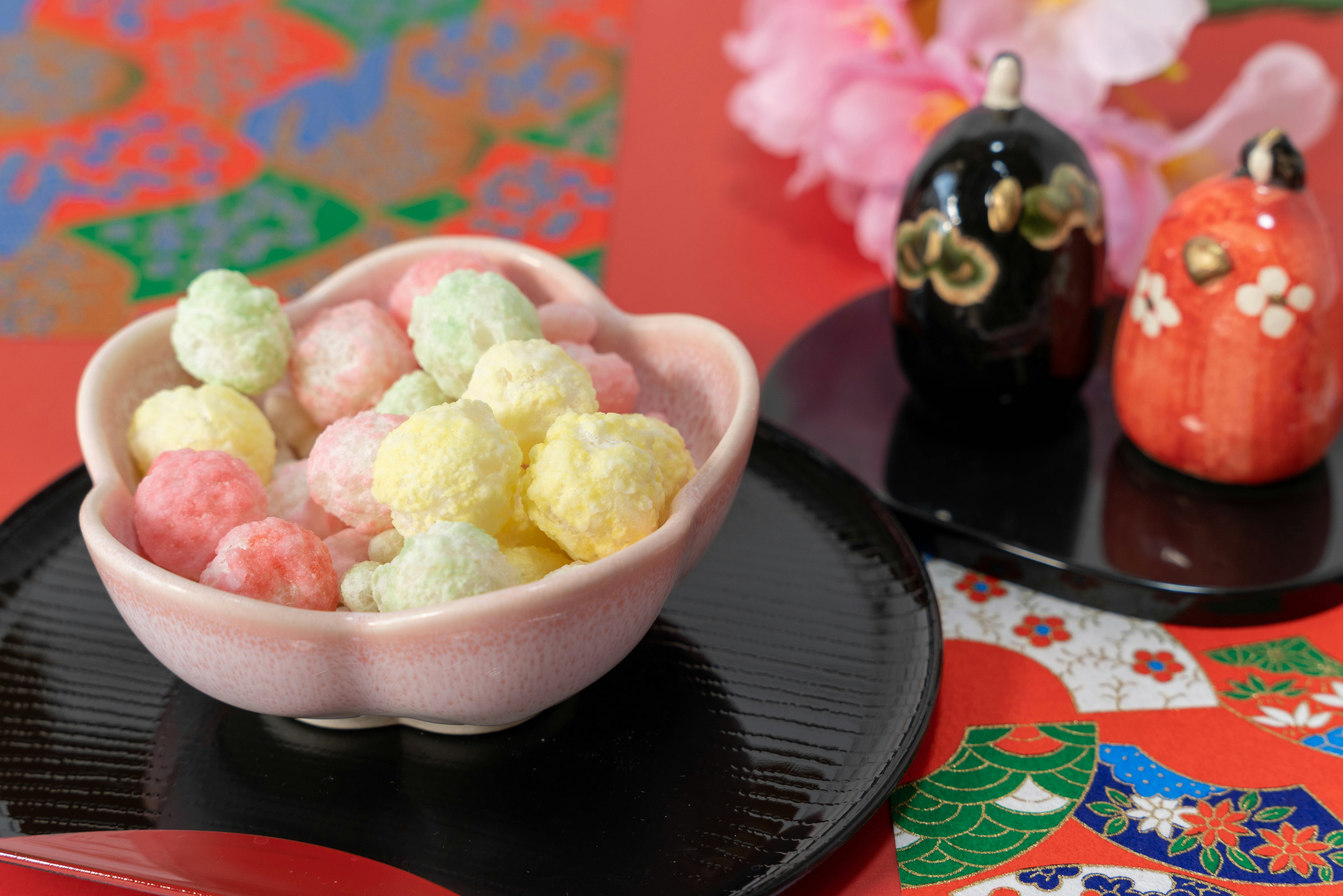 Dolci giapponesi tradizionali in una ciotola a forma di fiore rosa con bambole decorative e sfondo colorato