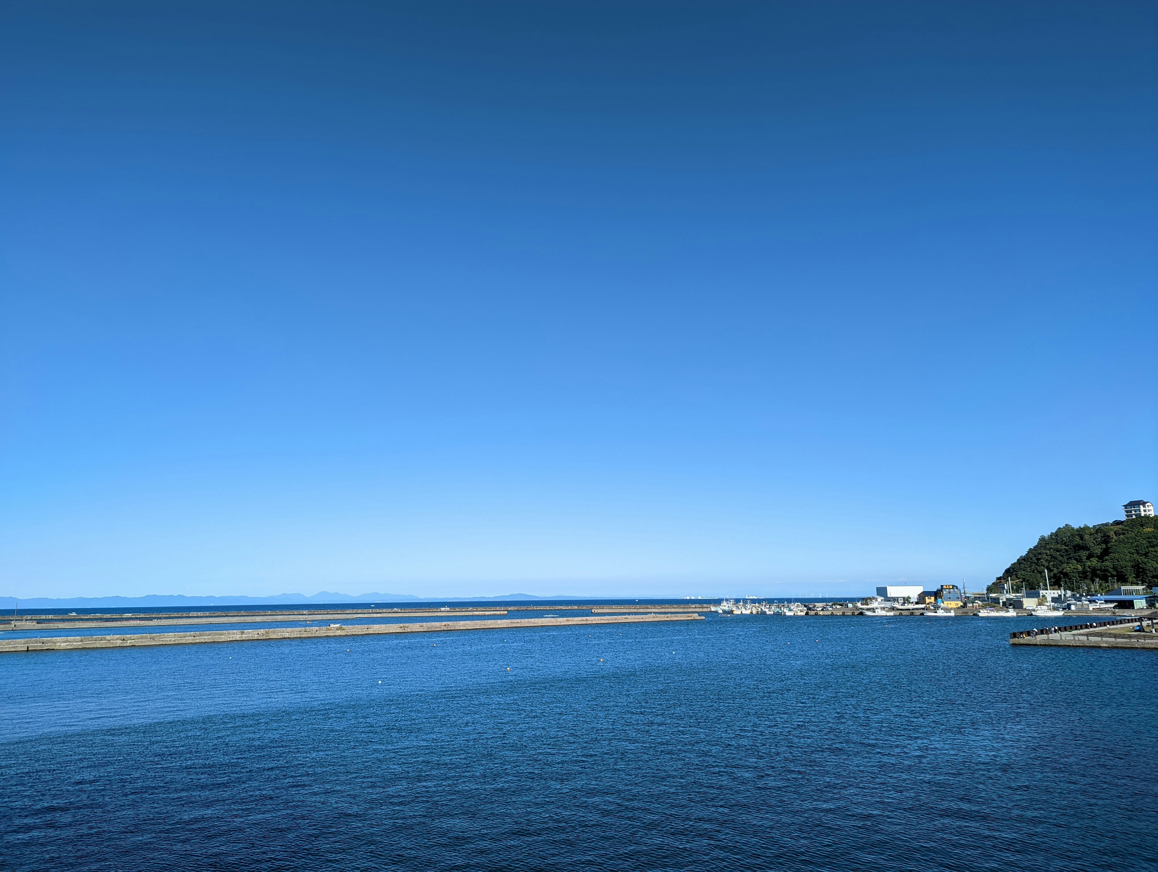 Un paesaggio sereno con cielo blu chiaro e mare calmo che presenta una piccola città costiera