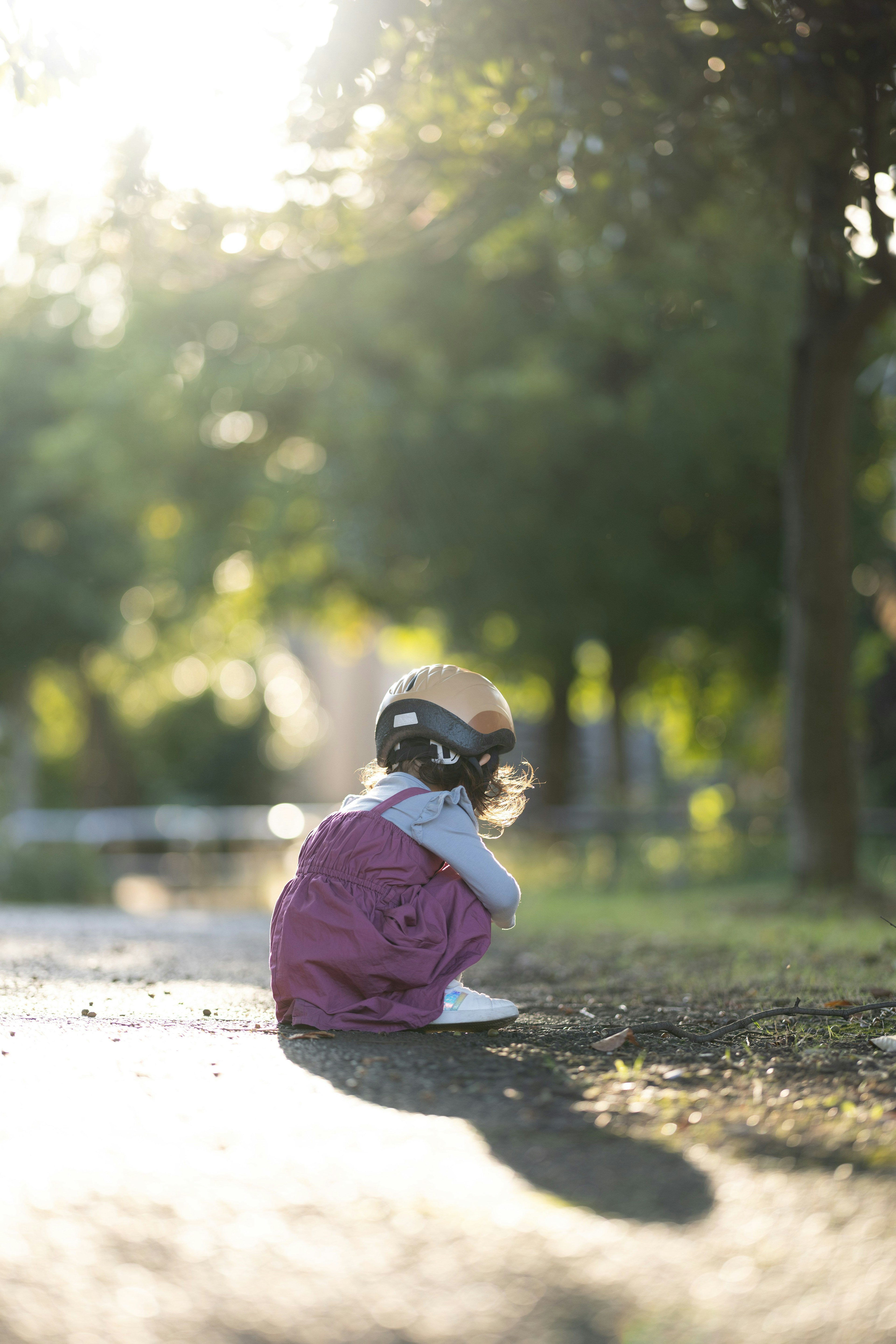 Niño sentado en un camino en un parque con luz solar filtrando a través de los árboles