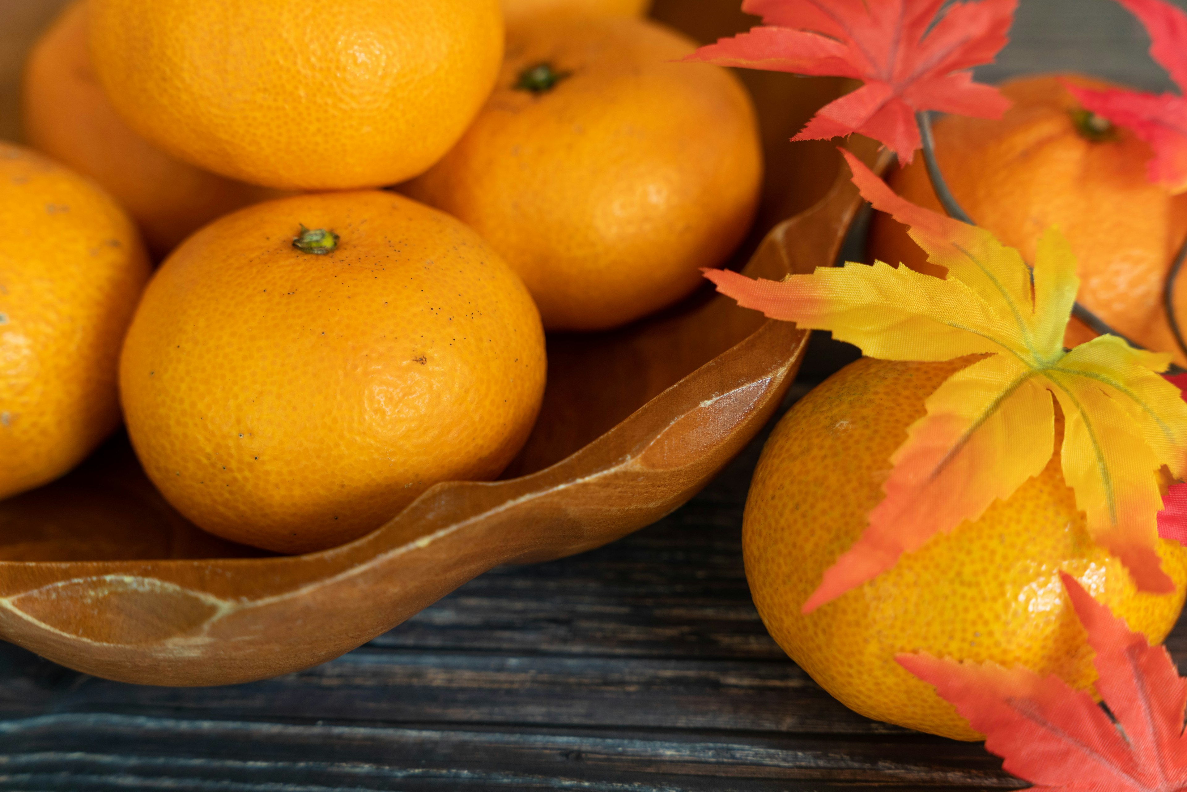 A wooden bowl filled with vibrant oranges and colorful autumn leaves