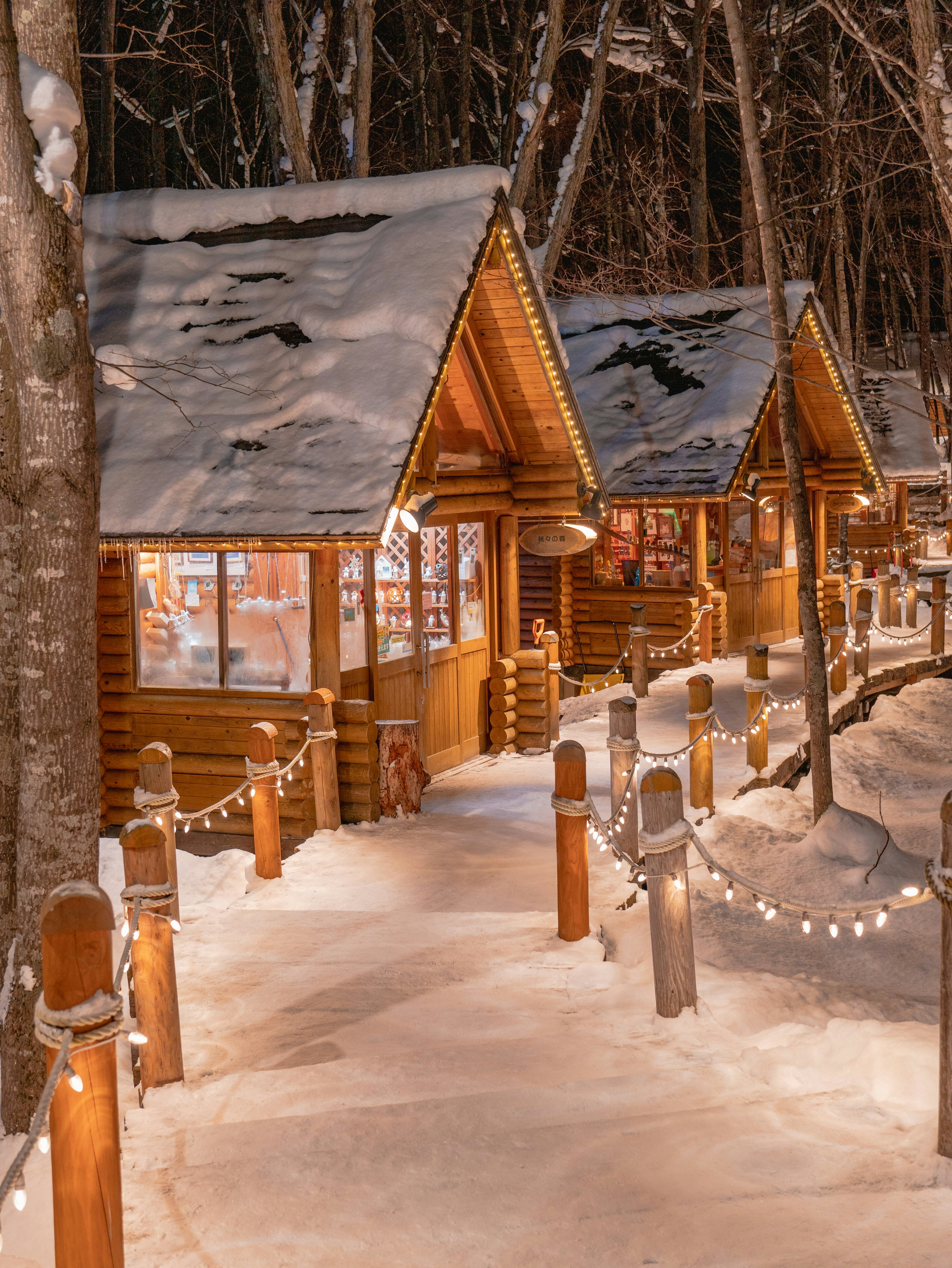 Cabañas de madera en un bosque nevado iluminadas por luces cálidas