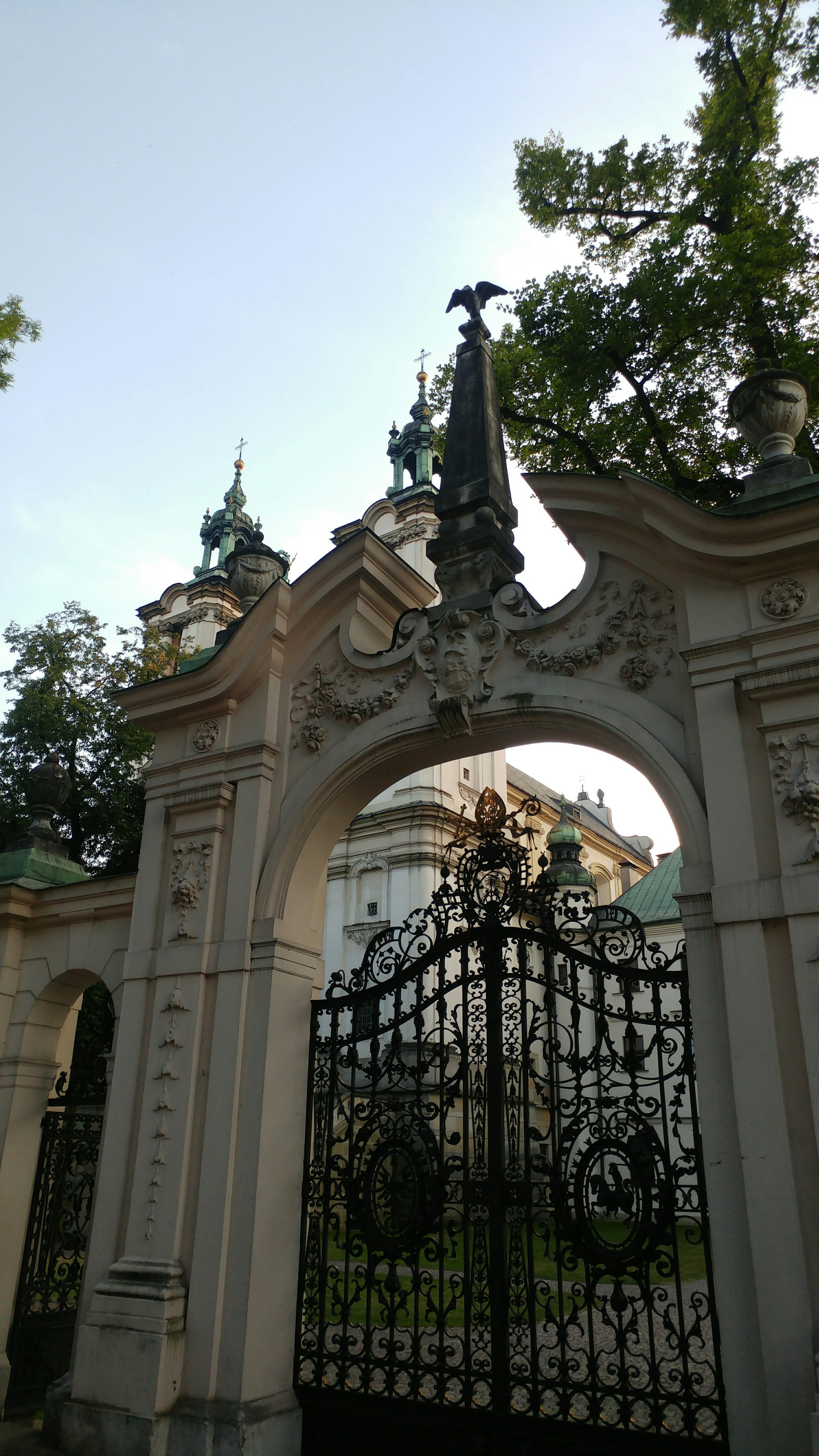 Decorative arch gate with intricate sculptures and a historic building in the background