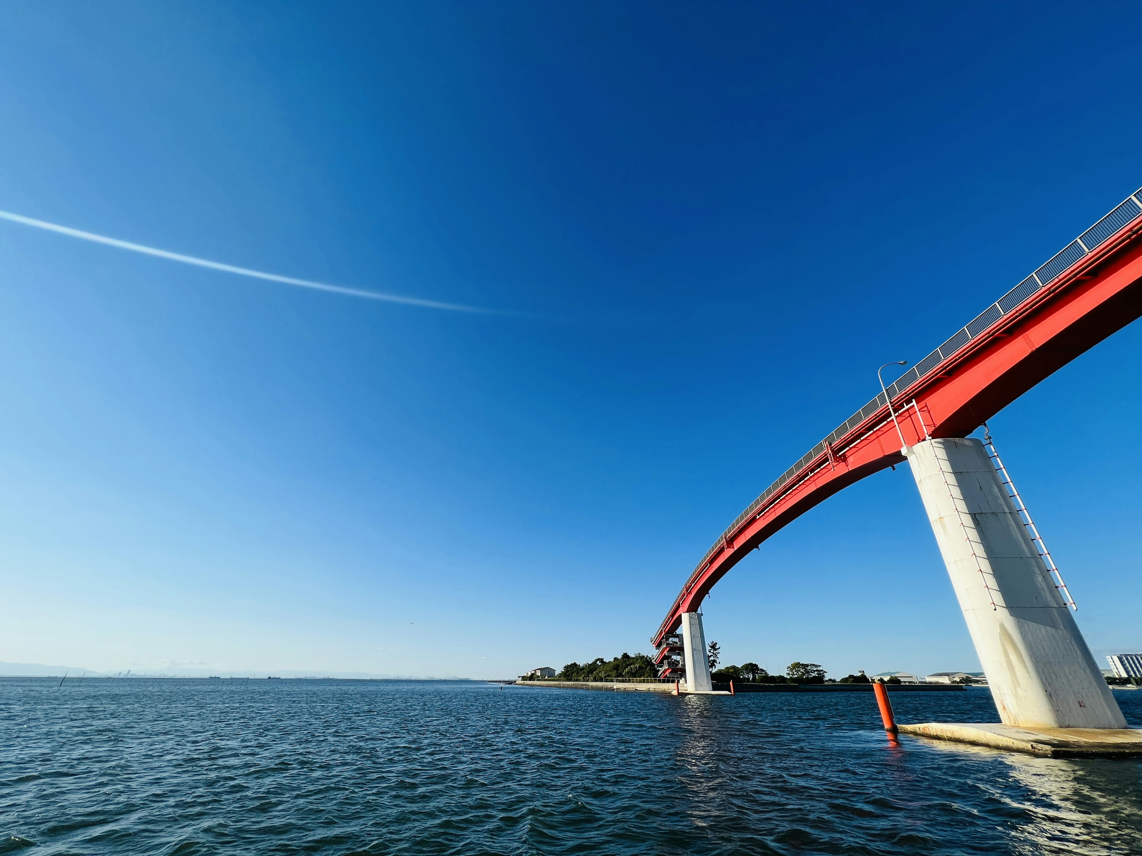 A red bridge arching over calm blue waters under a clear sky