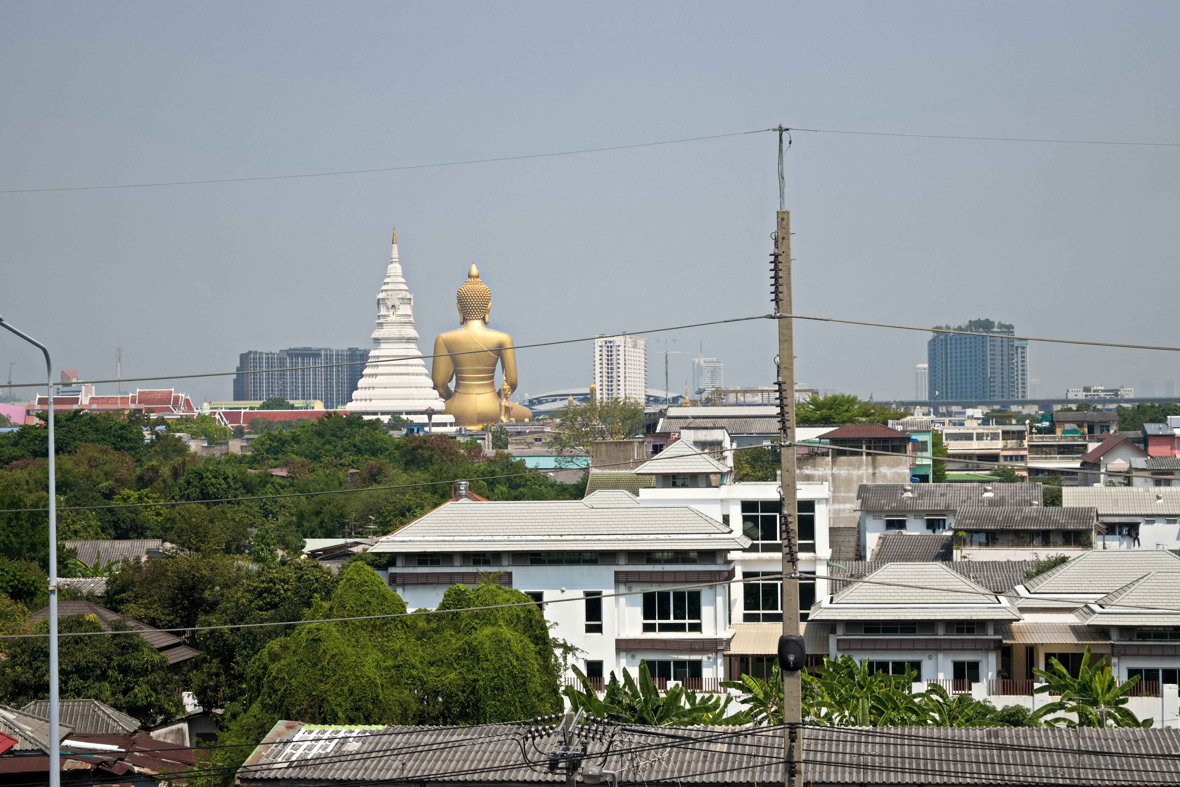 背景に巨大な金色の仏像と白い仏塔が見える都市の風景