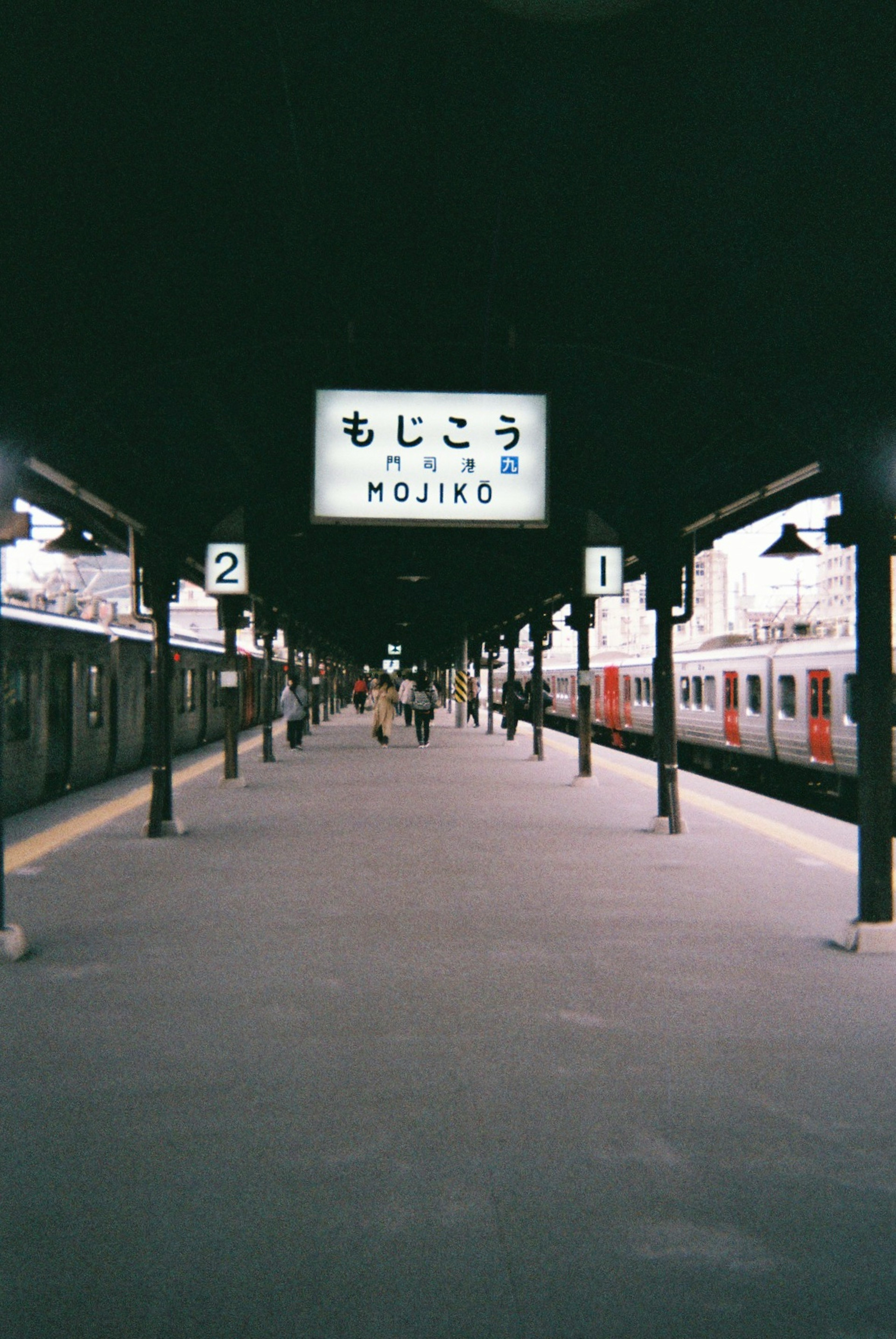 Piattaforma della stazione di Mojiko con treni e segnaletica