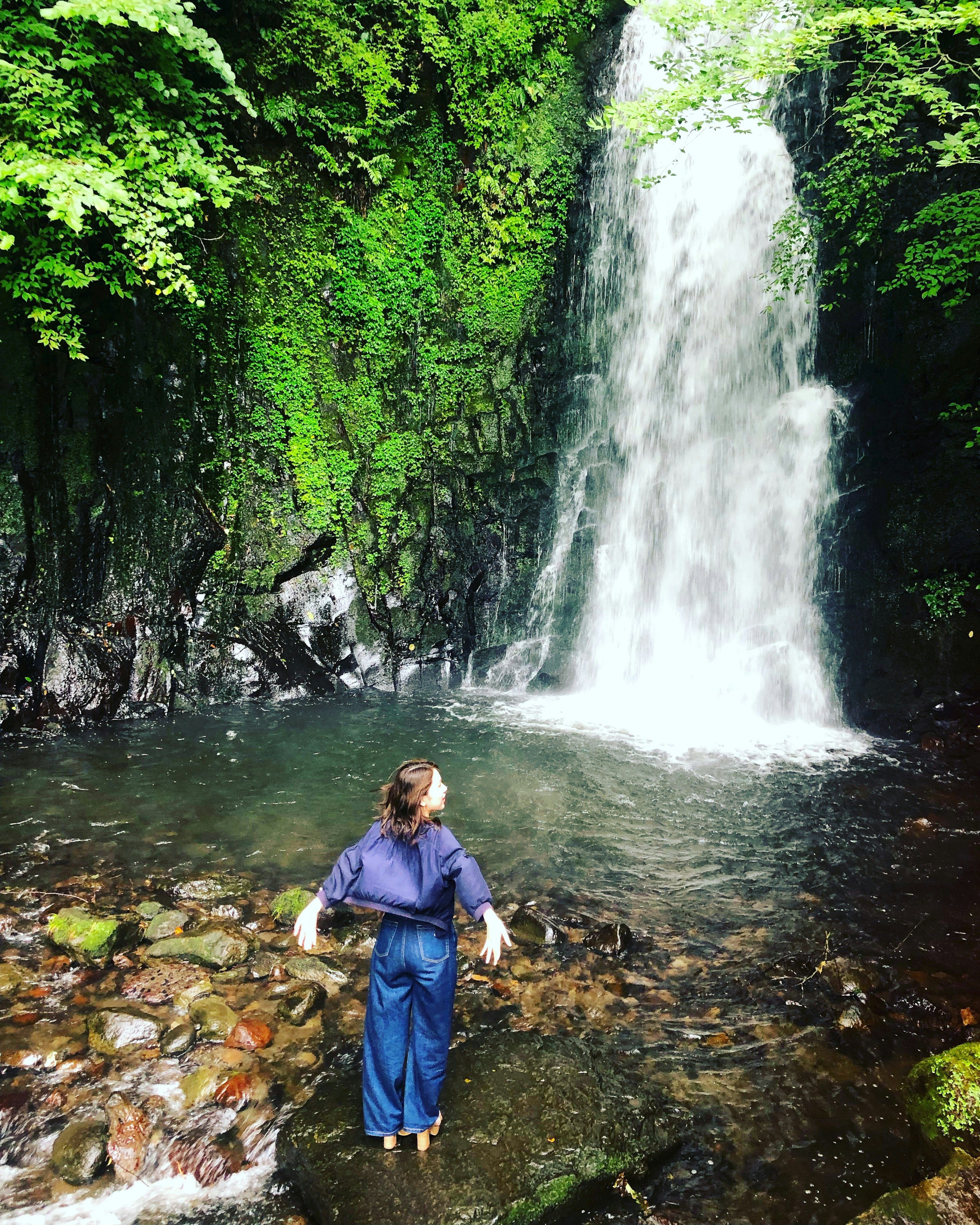 Frau steht vor einem Wasserfall umgeben von üppigem Grün