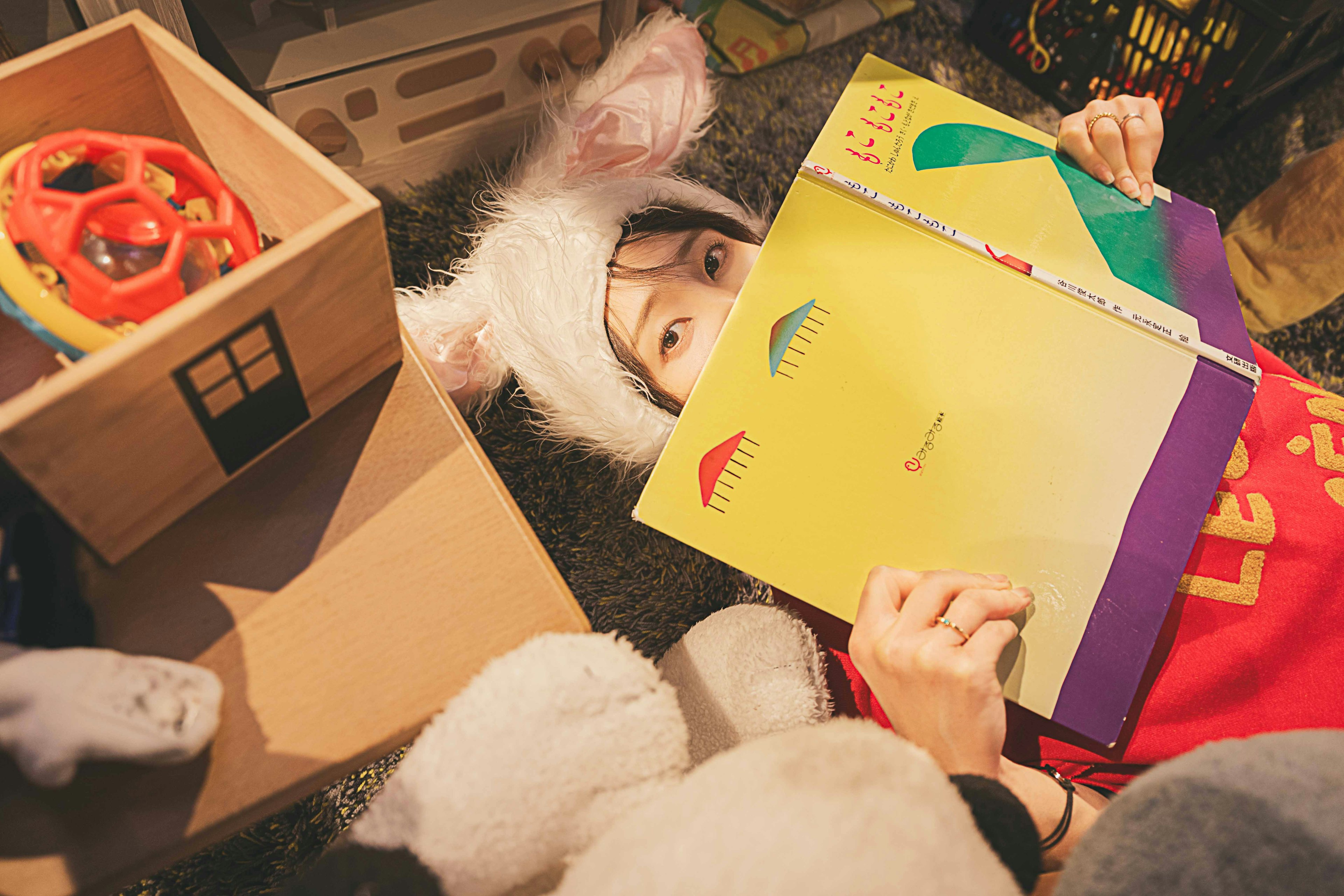 Child wearing a rabbit hat reading a colorful book on the floor