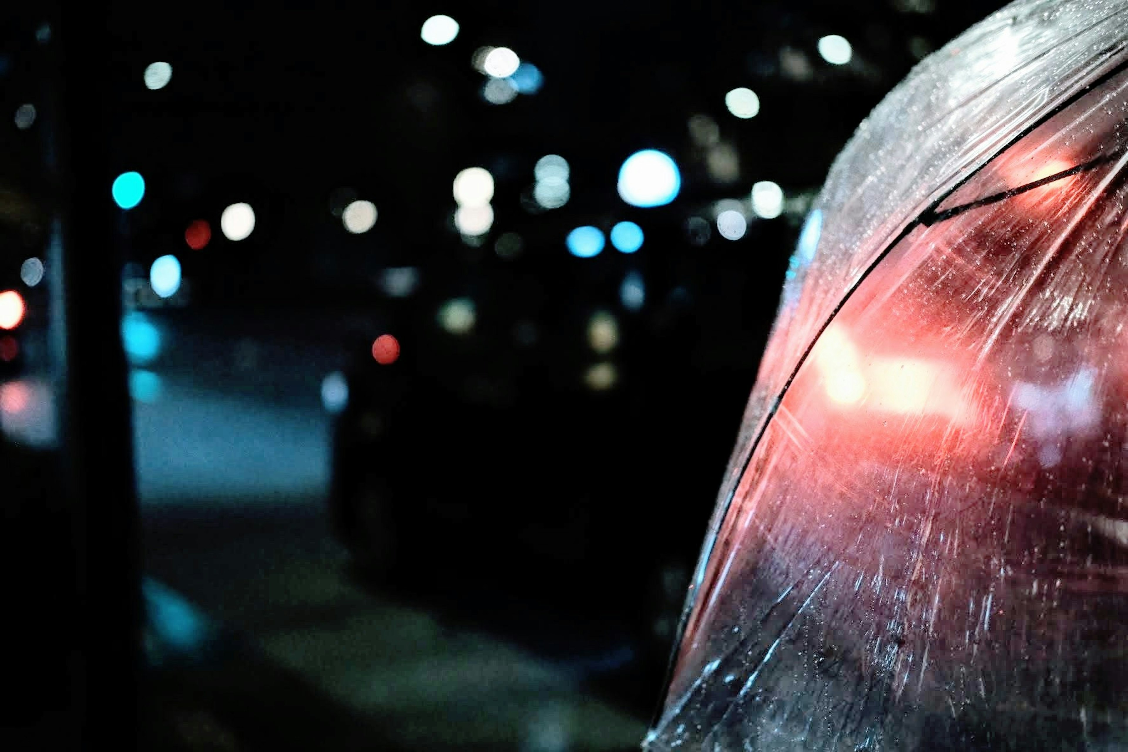 Night city scene featuring a close-up of a wet umbrella with a red taillight in the background