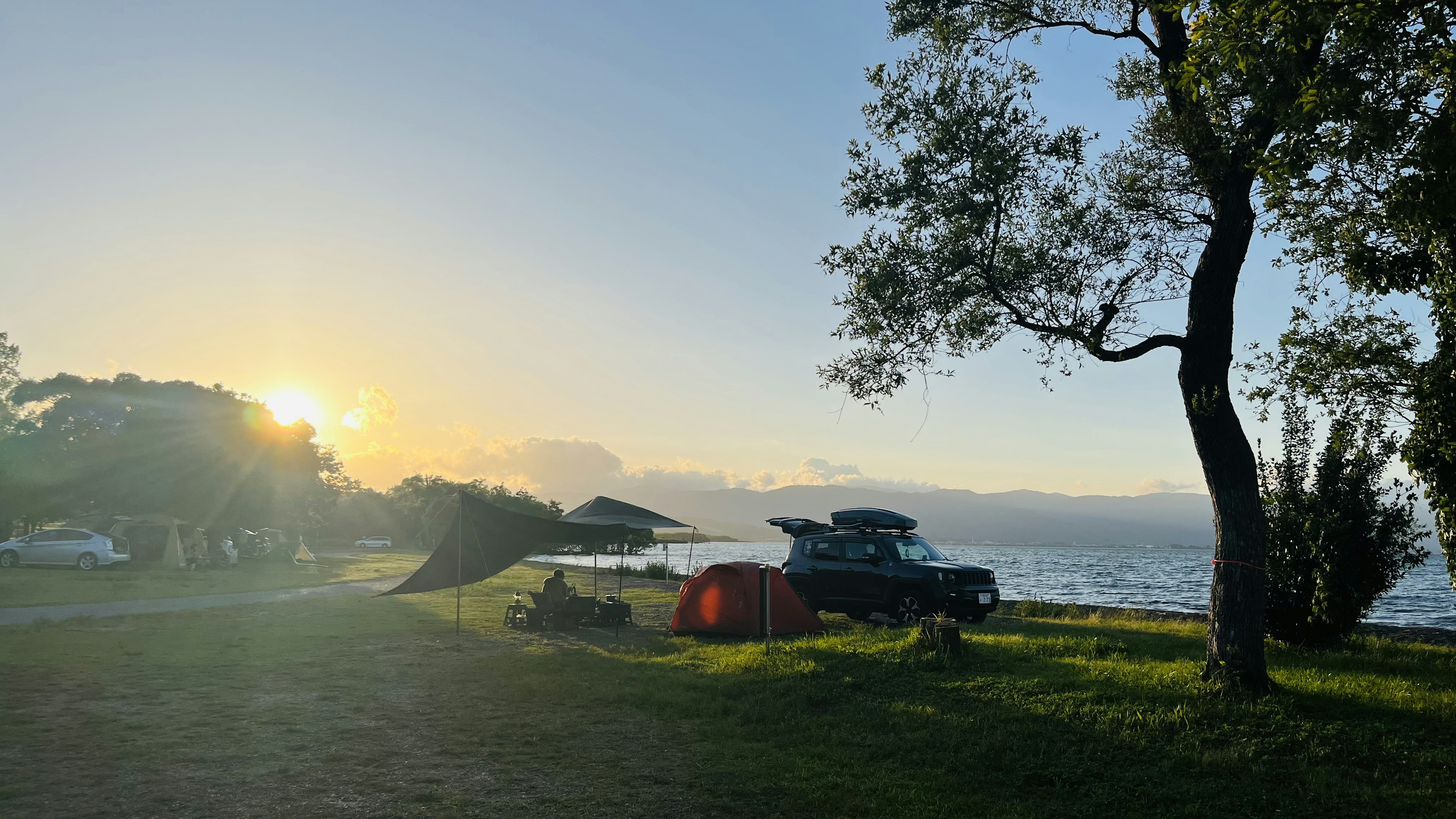 湖畔のキャンプサイトにテントと車があり、夕日が美しい光景