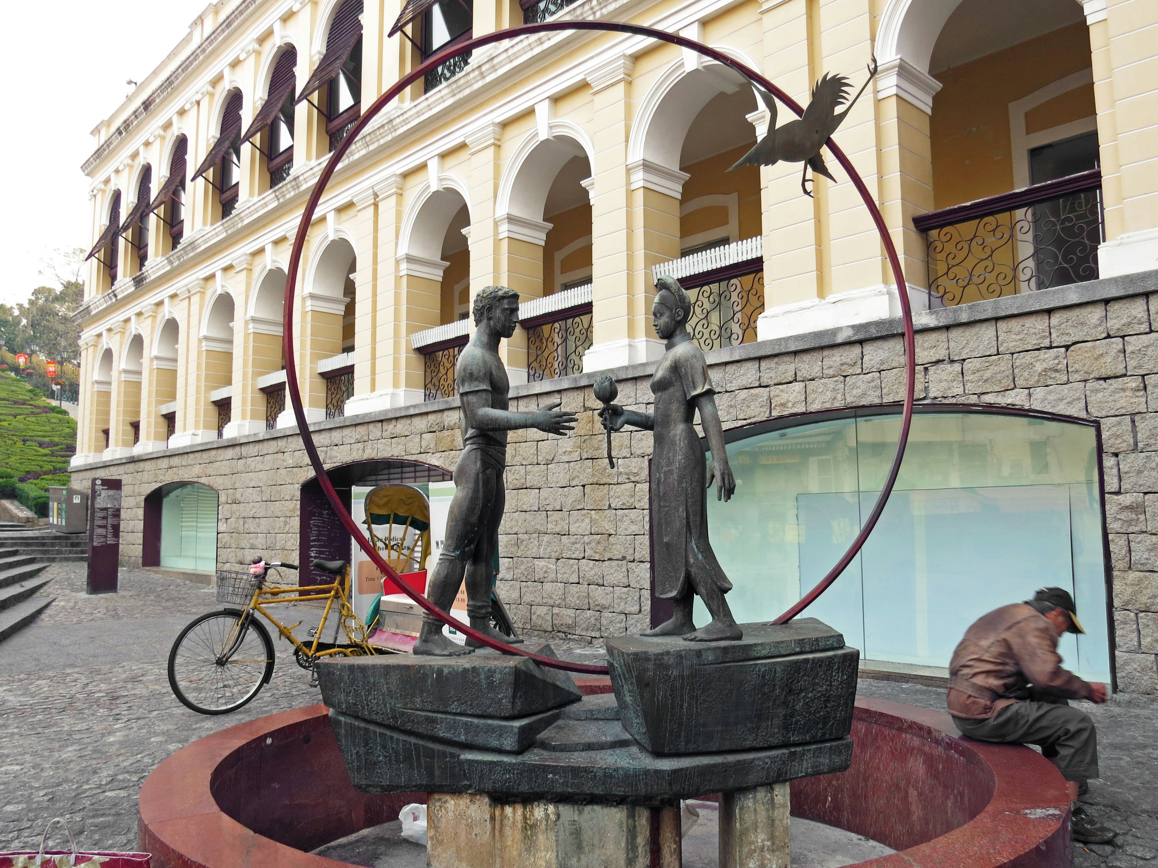 Escultura de dos figuras estrechándose la mano en un marco circular con una bicicleta cerca