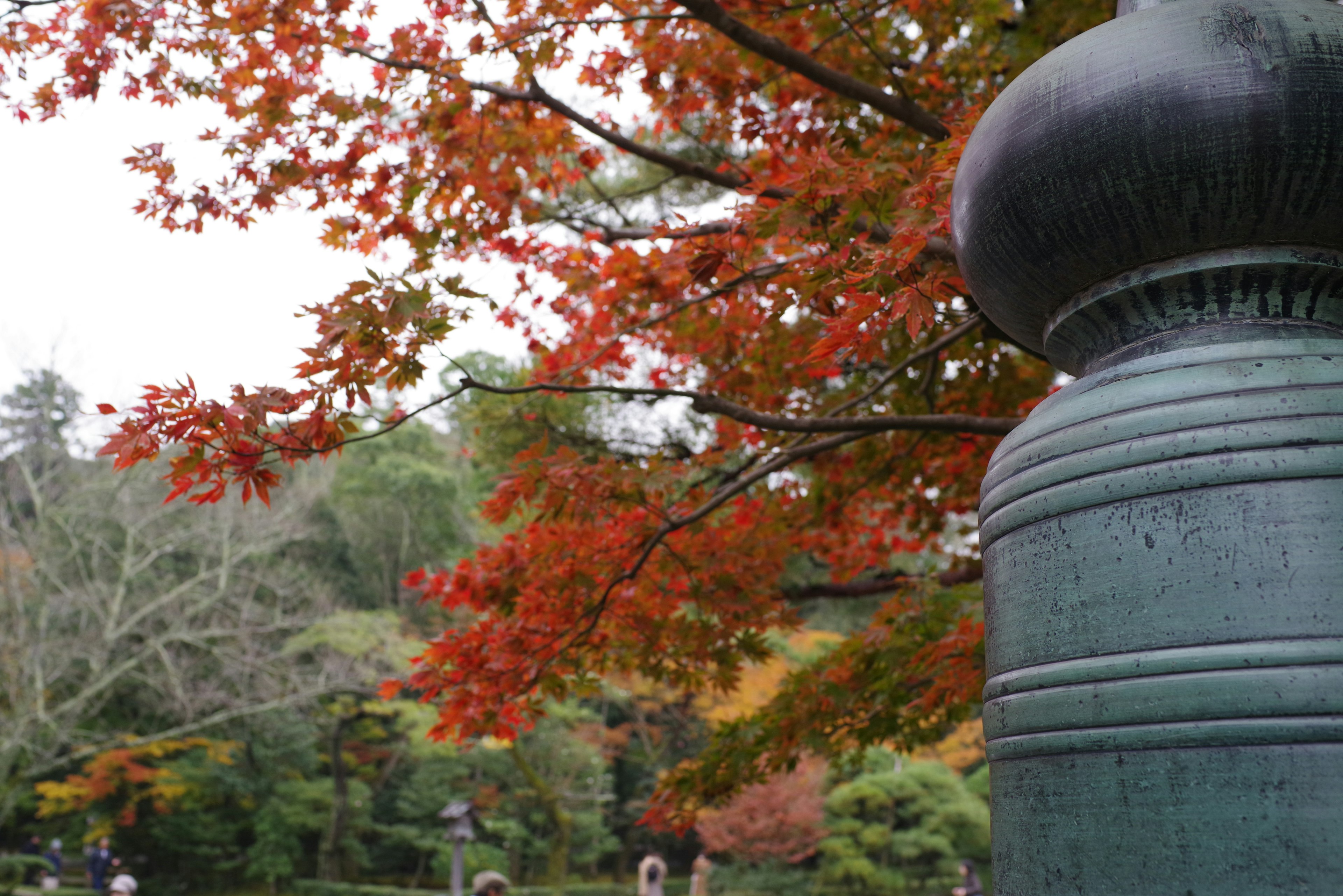 A landscape featuring autumn foliage and a bronze lantern