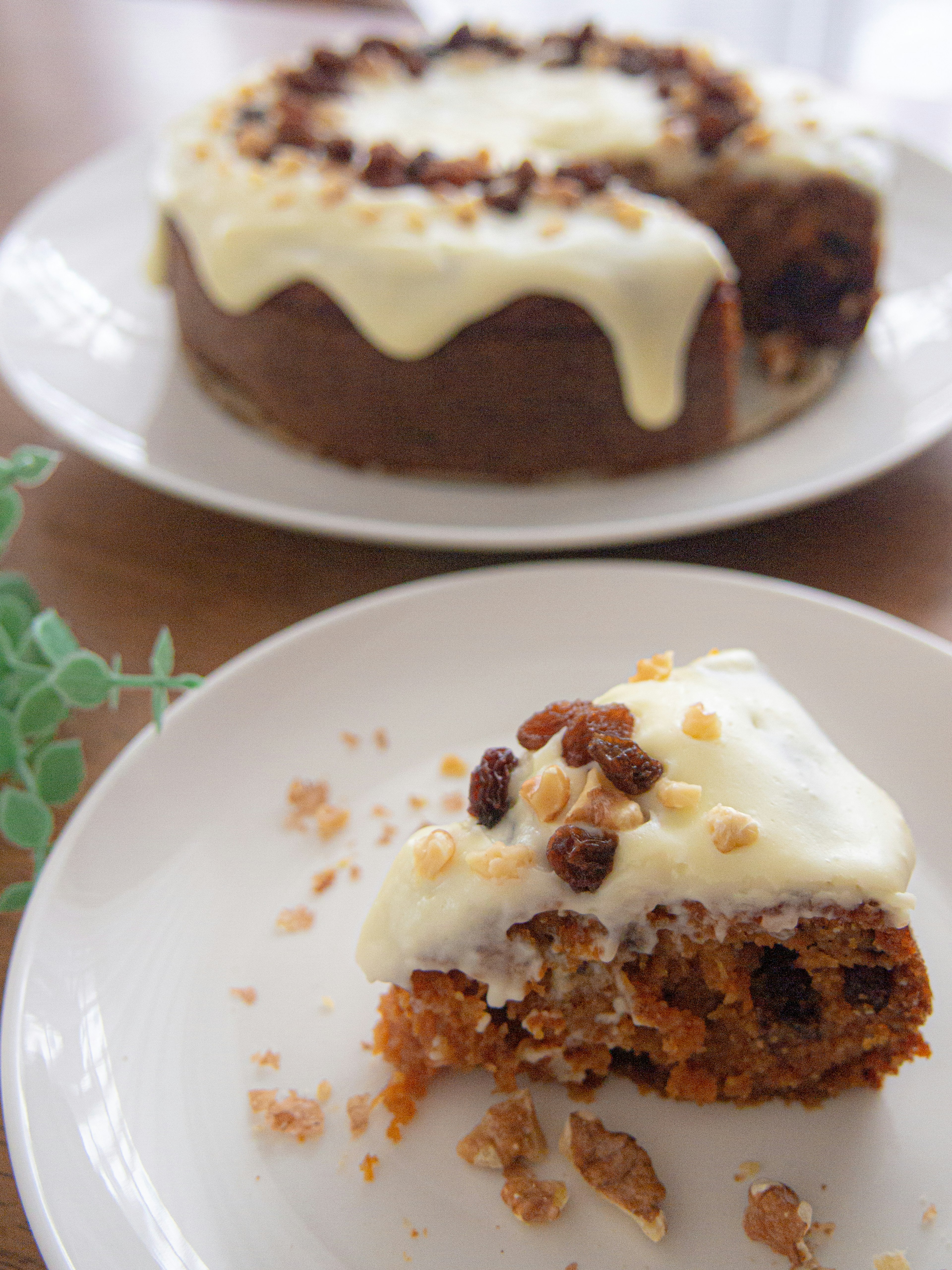 Slice of carrot cake with cream cheese icing and the whole cake in the background