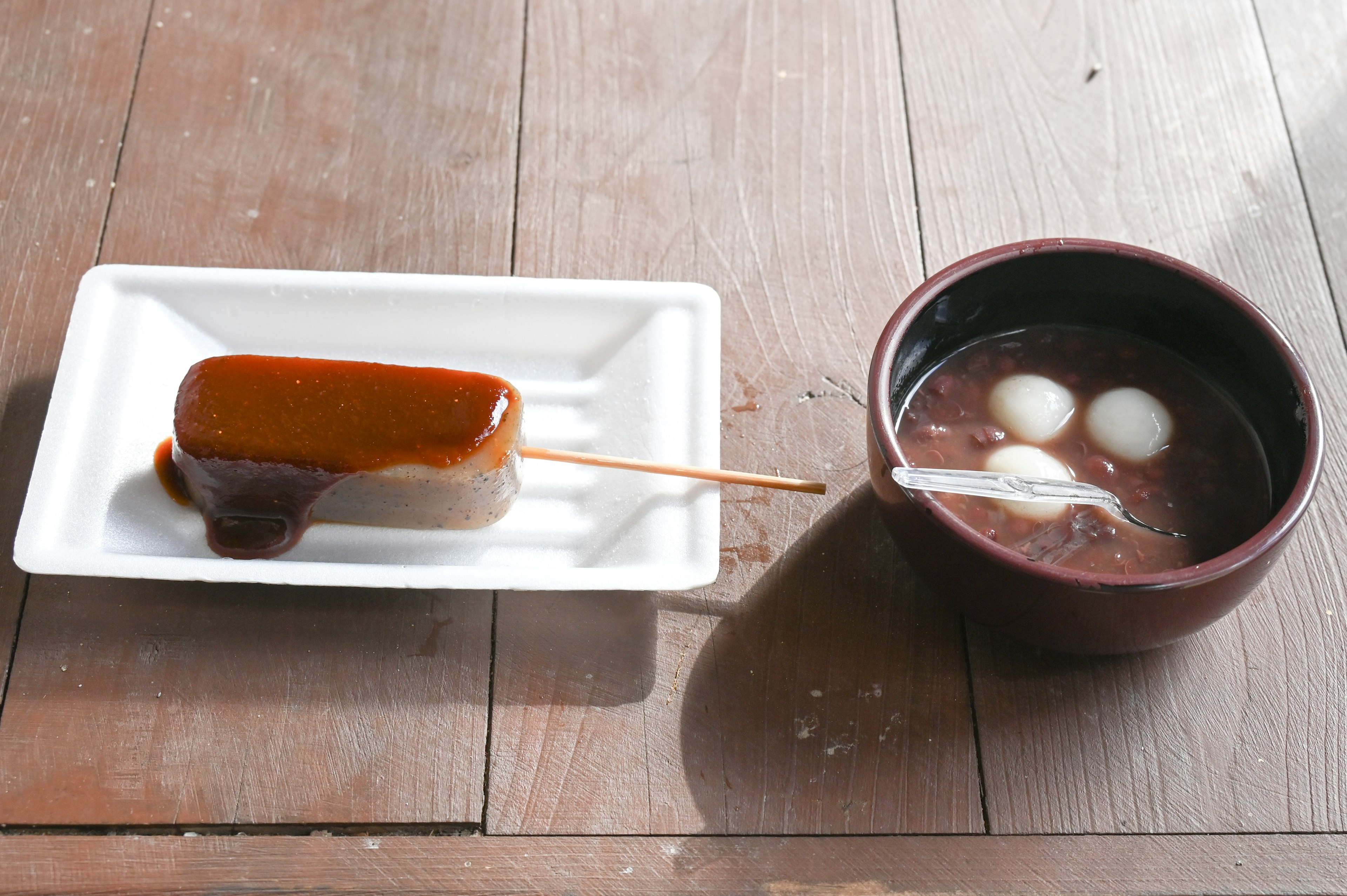 Postre en brocheta cubierto con salsa dulce junto a un tazón de sopa de mochi