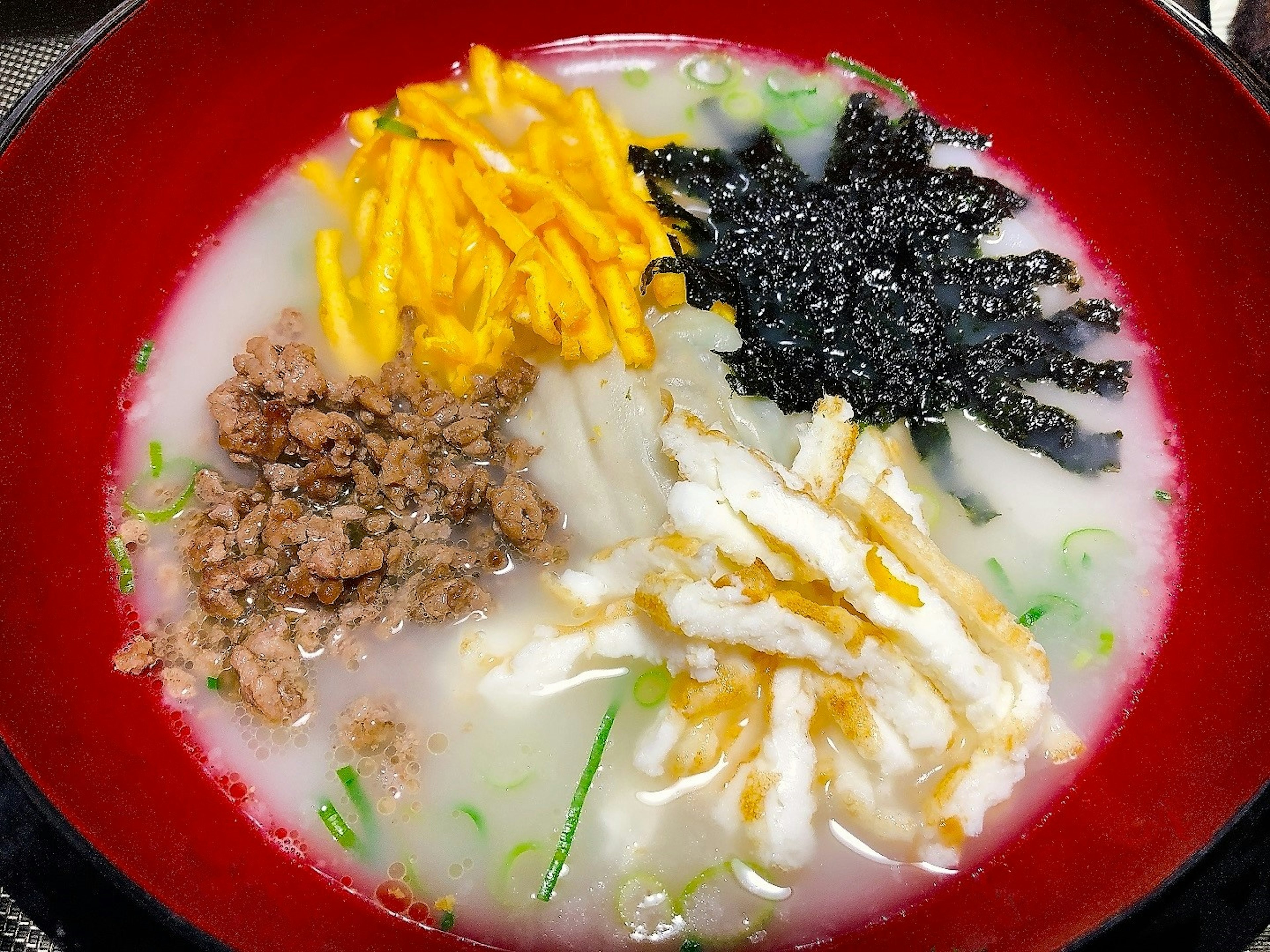 Korean soup dish topped with noodles vegetables and minced meat in a red bowl