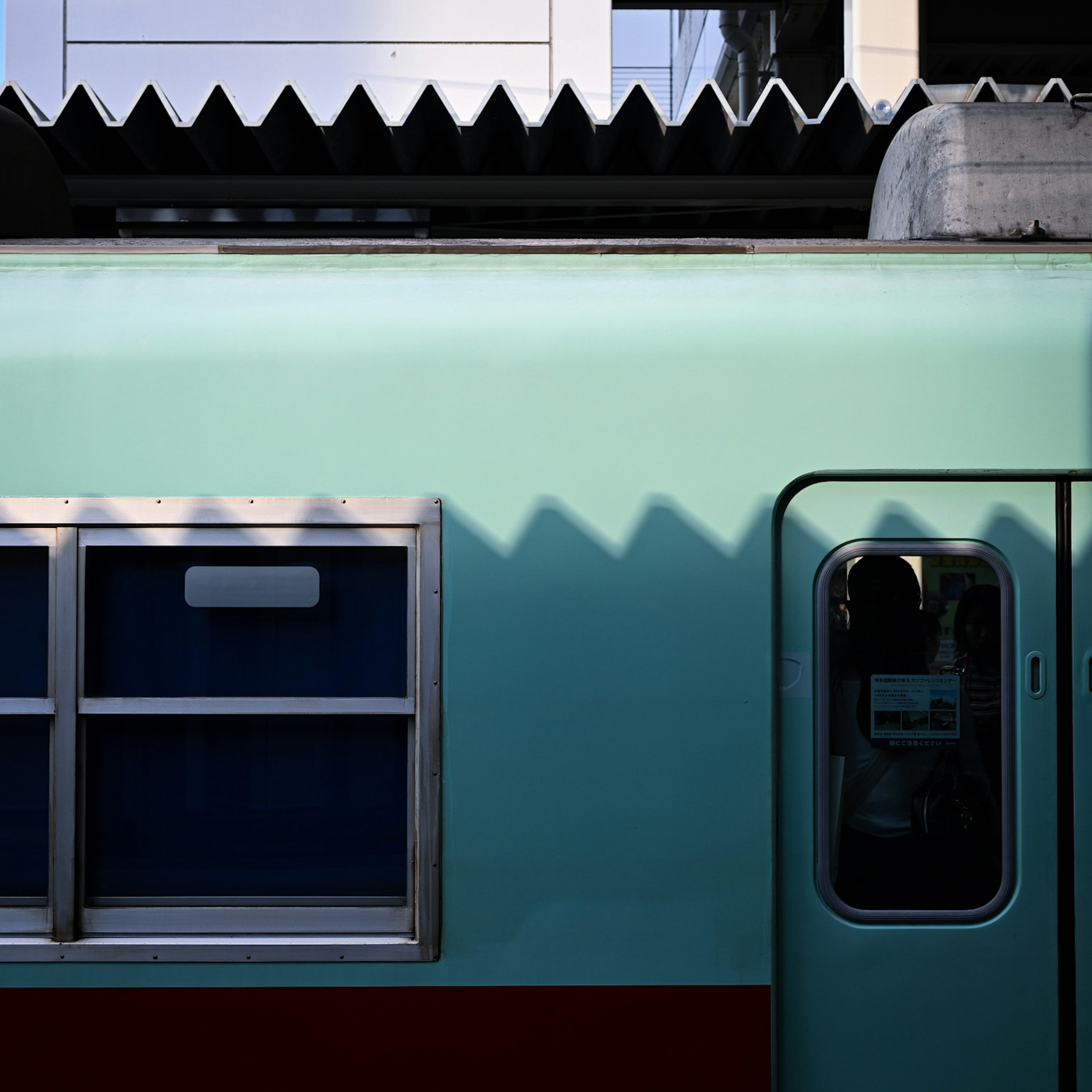 Close-up of a teal train car featuring windows and a door with shadow patterns