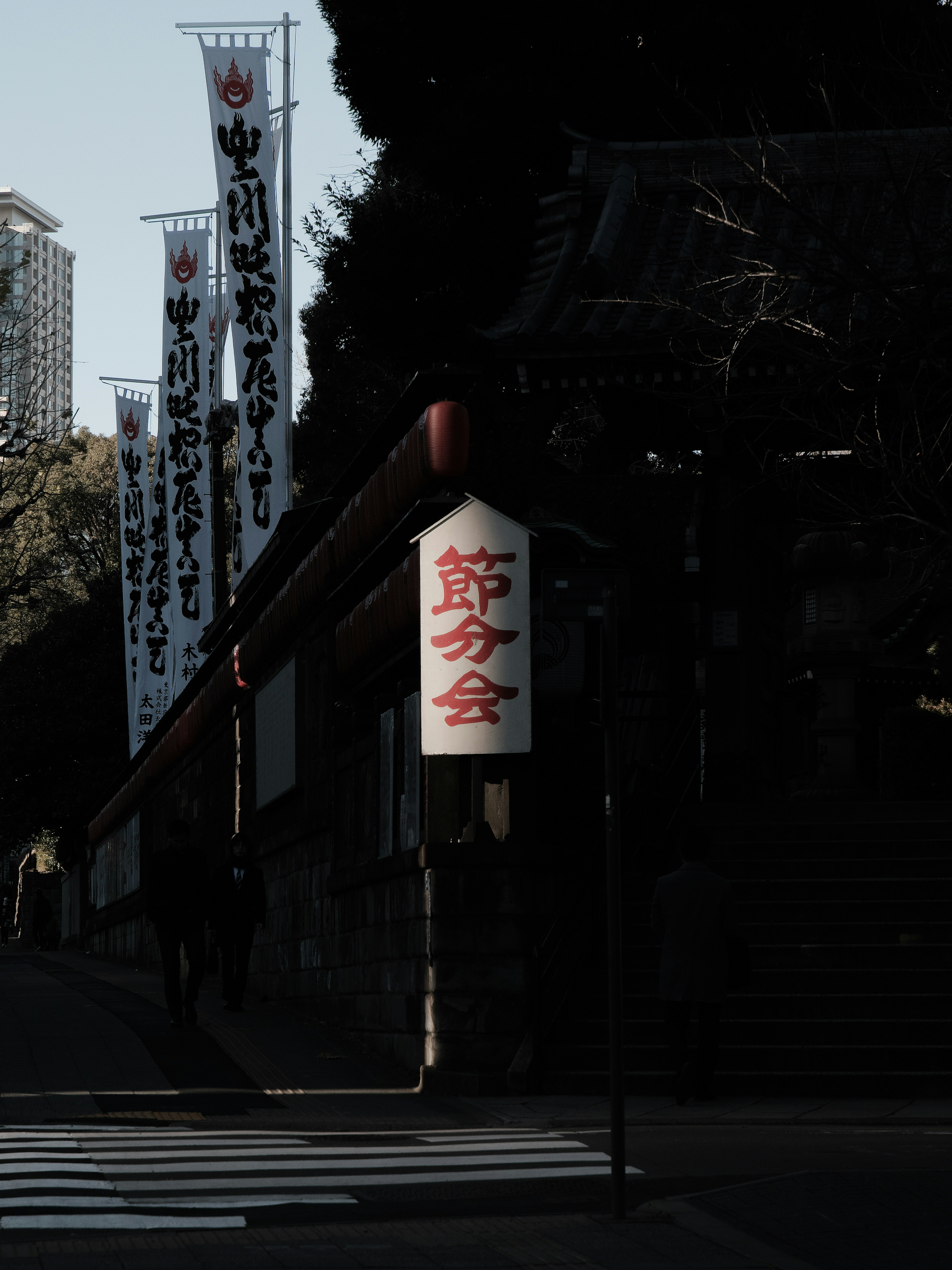 Schild eines japanischen Tempels mit Bannern in einer dunklen Umgebung